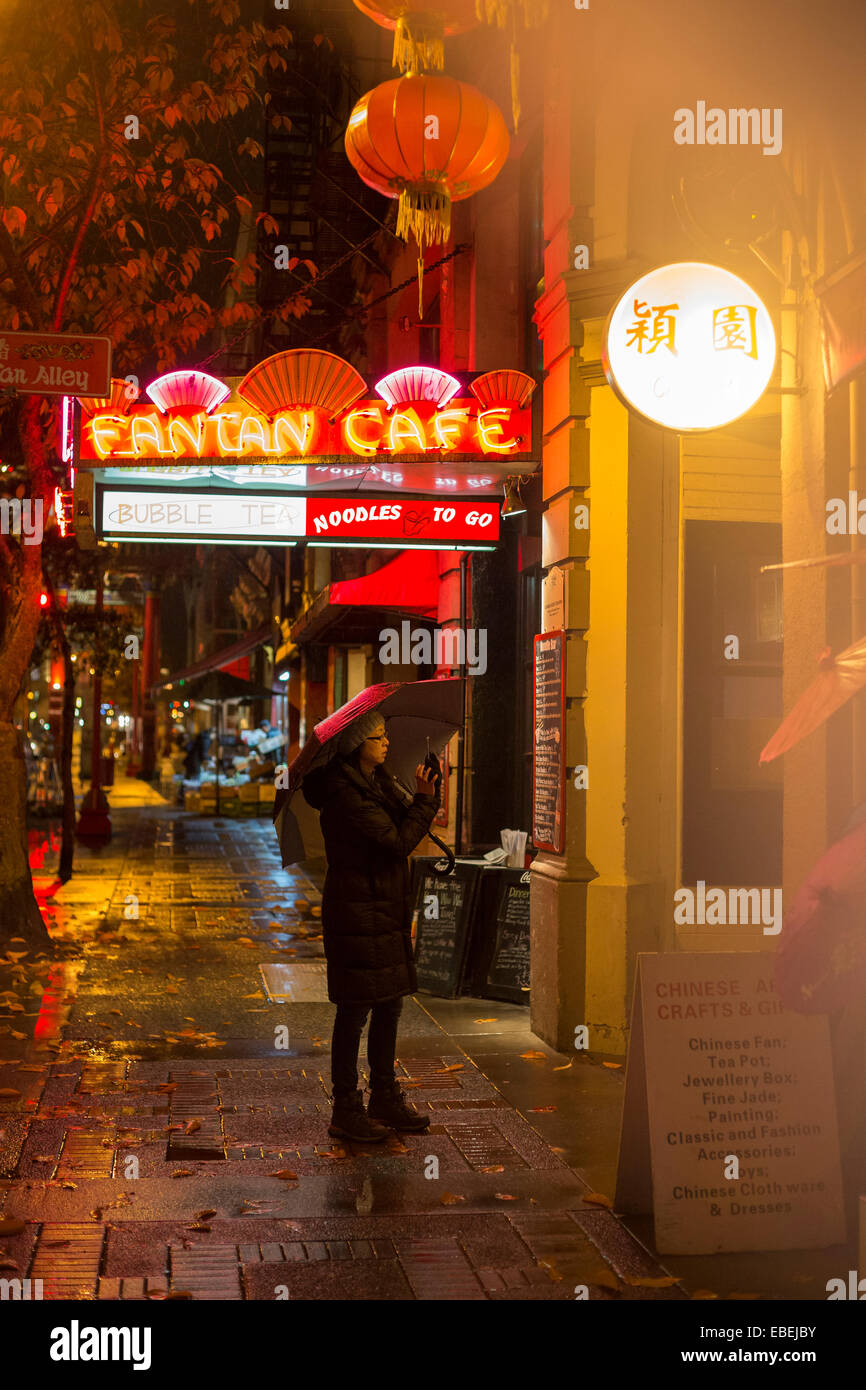 Chinese woman photographing Fan Tan alley entrance in Chinatown on rainy night-Victoria, British Columbia, Canada. Stock Photo