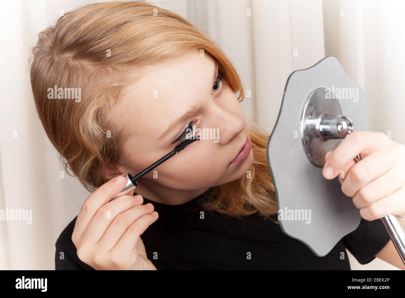Blond beautiful Caucasian girl in black paints eyelashes with mascara Stock Photo