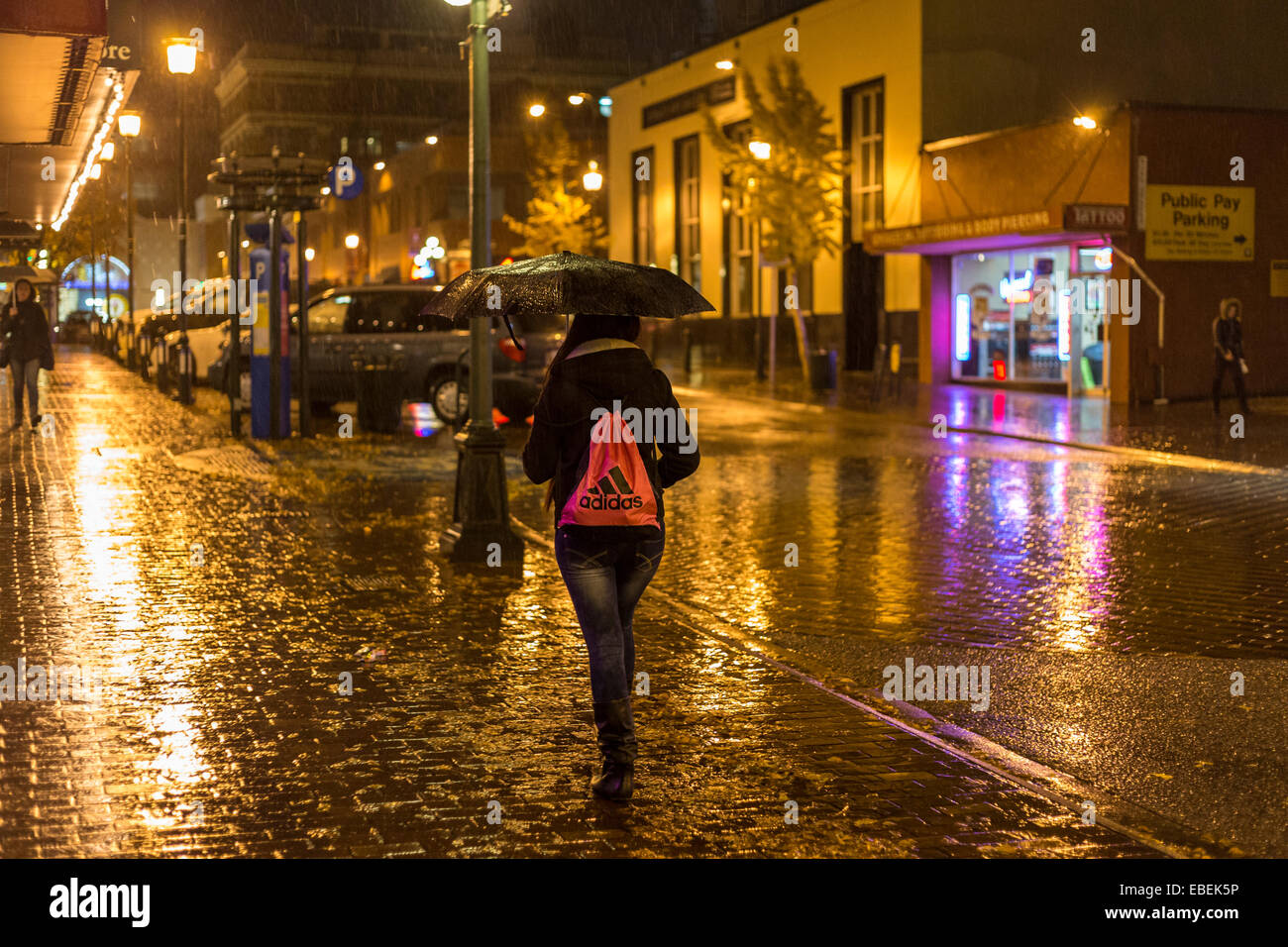 Young woman walking through downtown on rainy night-Victoria, British Columbia, Canada. Stock Photo