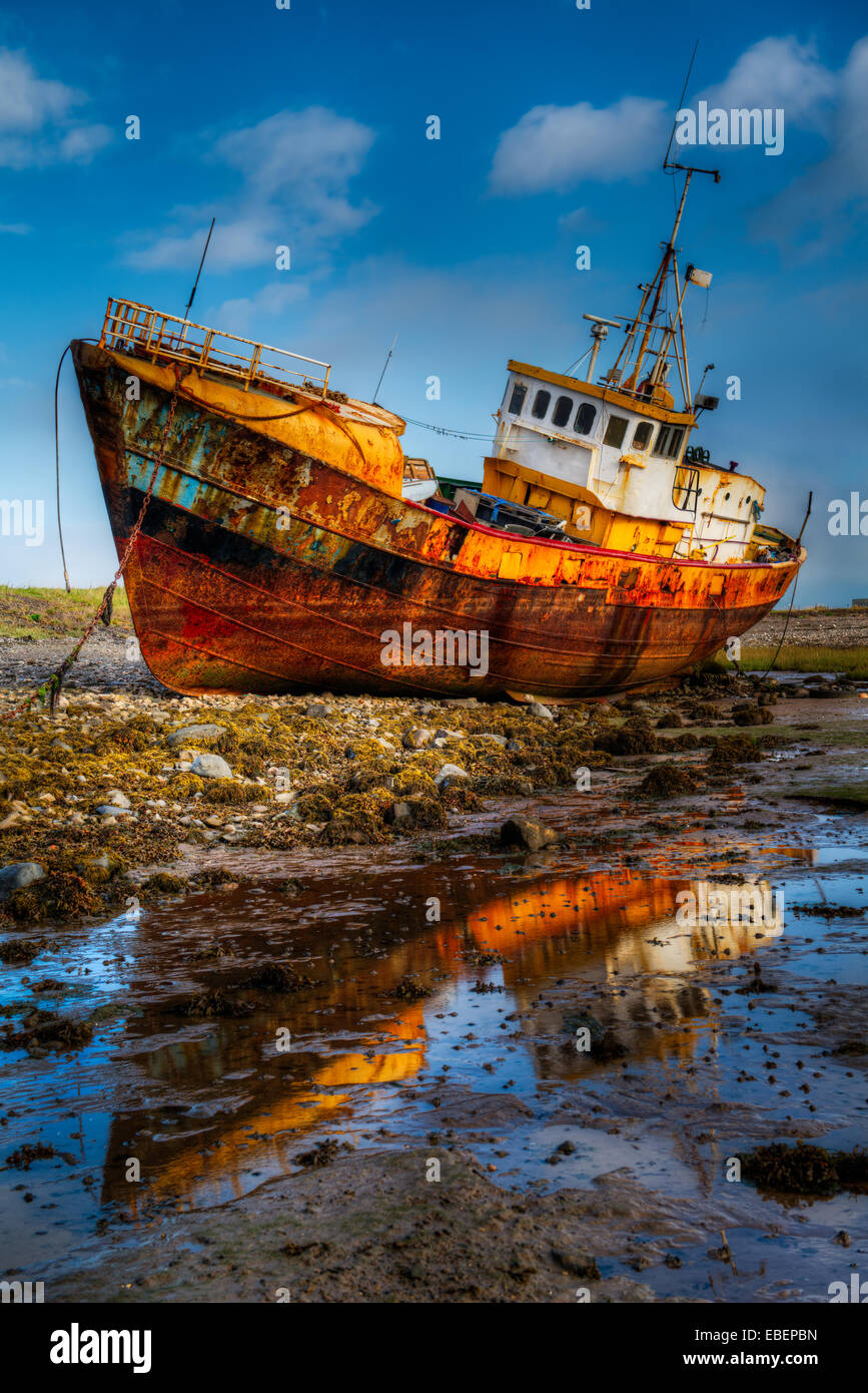 An approximate 30 meter Steel fishing boat sitting on the bottom during low tide on a bright cloudy blue sky day. Stock Photo