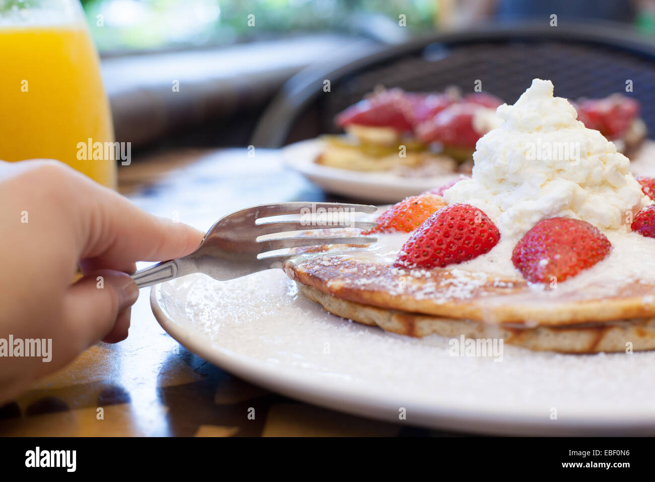 Hand cutting strawberry pancakes with fork Stock Photo