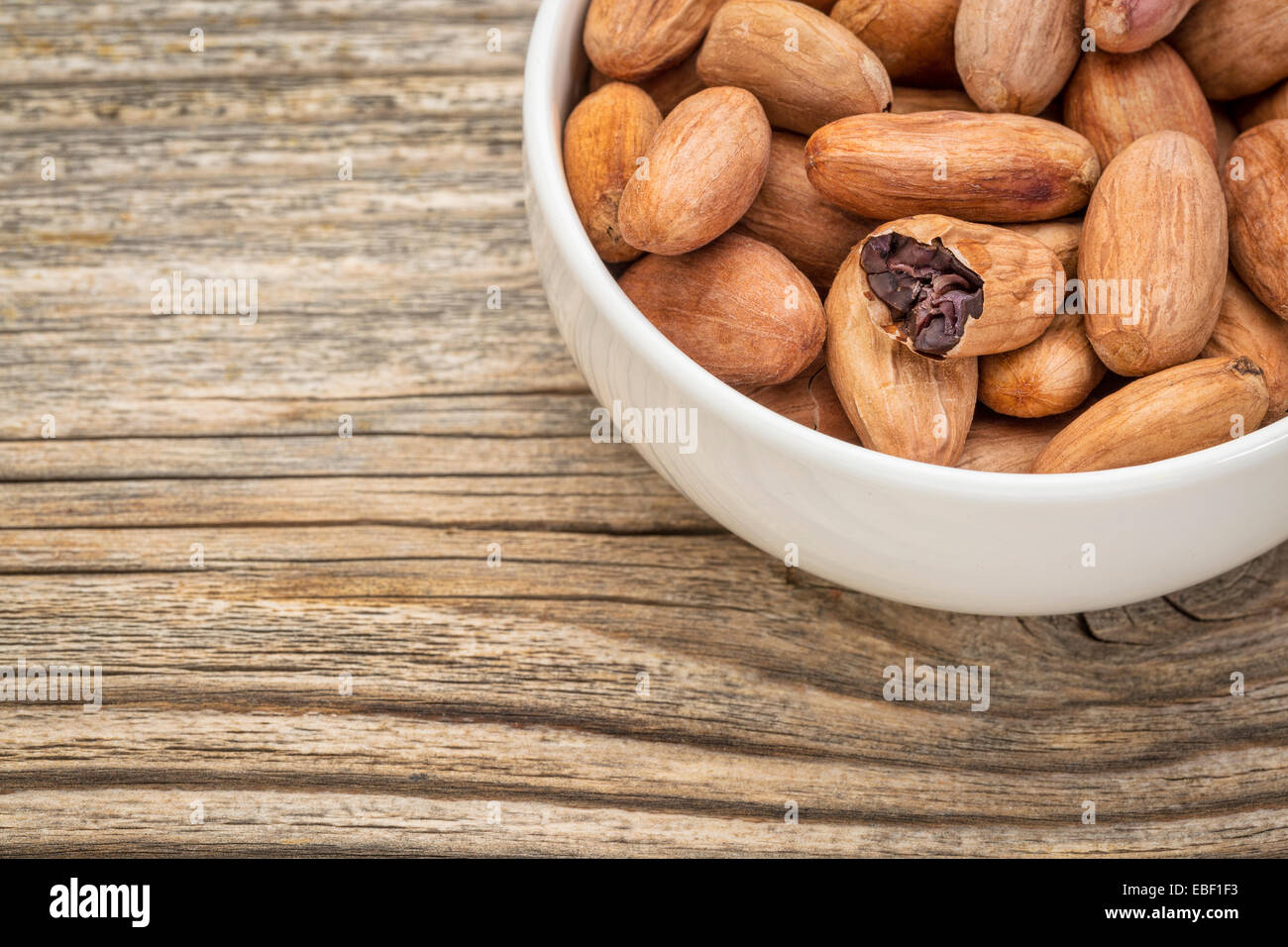 bowl of raw organic cacao beans  against grained wood Stock Photo