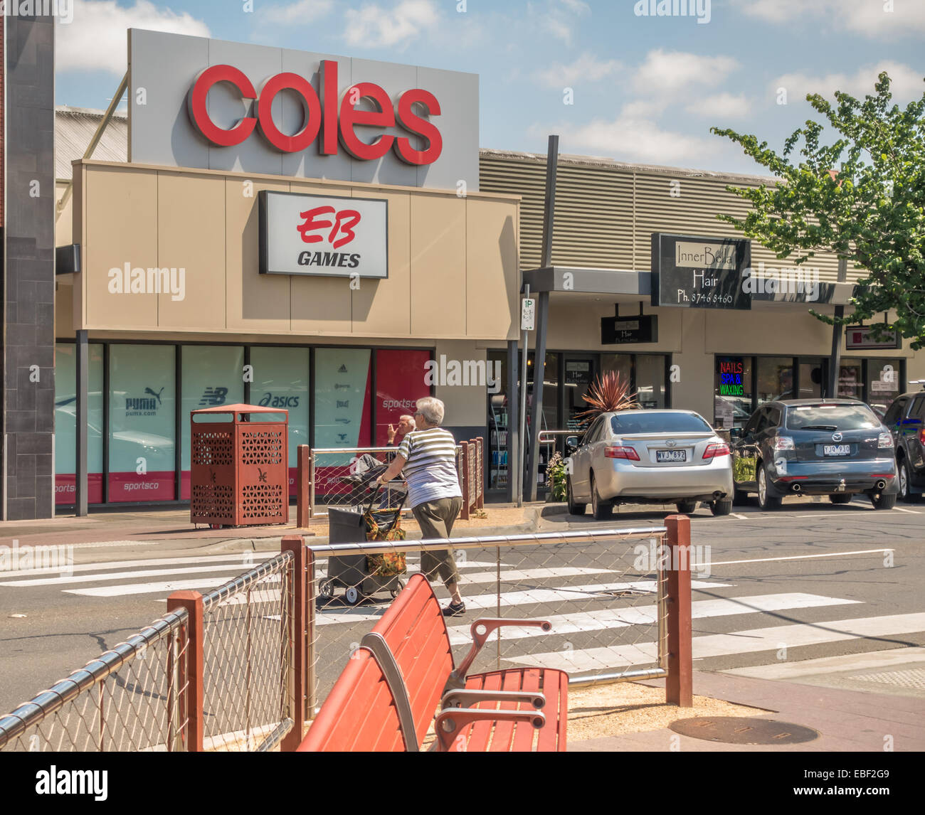 Senior woman crossing street under Coles and EB store signs in Sunbury, Victoria, Australia Stock Photo