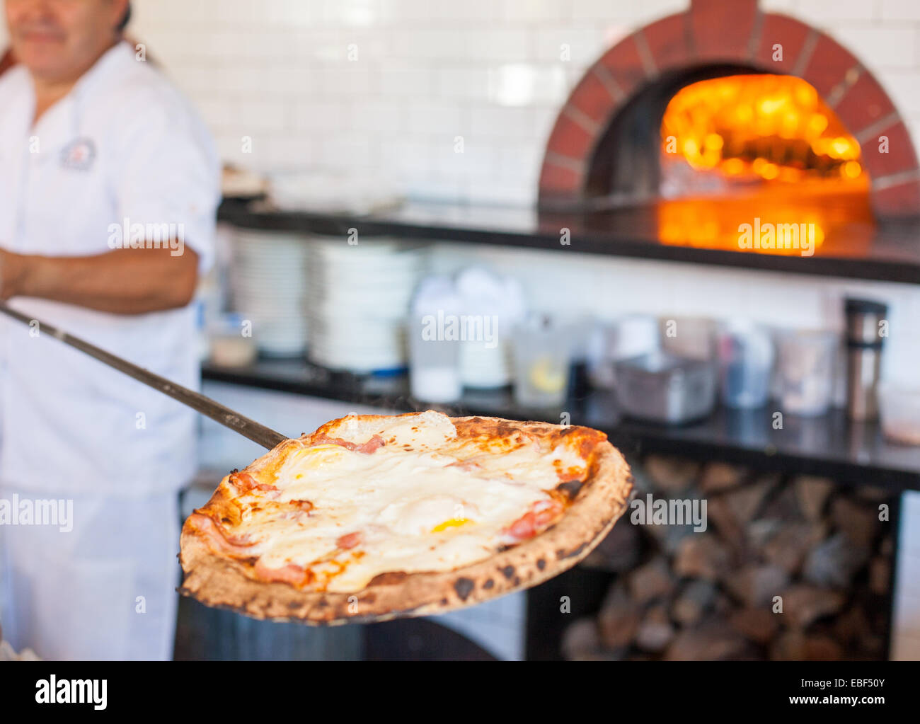 Man pulling pizza paddle out of a wood burning oven Stock Photo