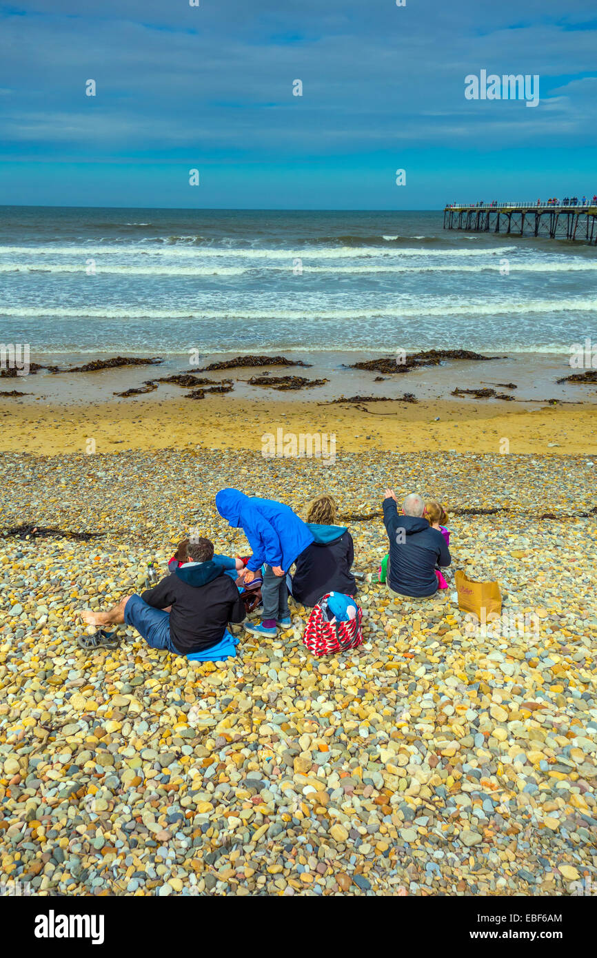 Family sat on pebbly beach scene, Saltburn by the Sea, holiday resort Stock Photo