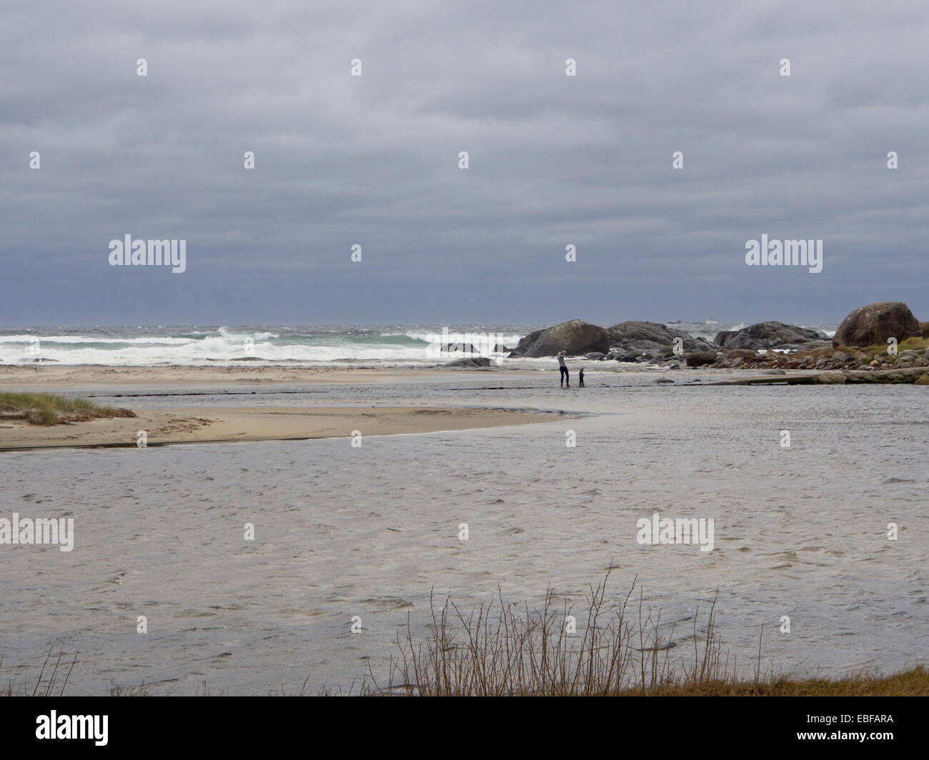 Autumn or winter storms on Jaeren, west coast of Norway near Stavanger waves breaking over stones and beach two people in water Stock Photo