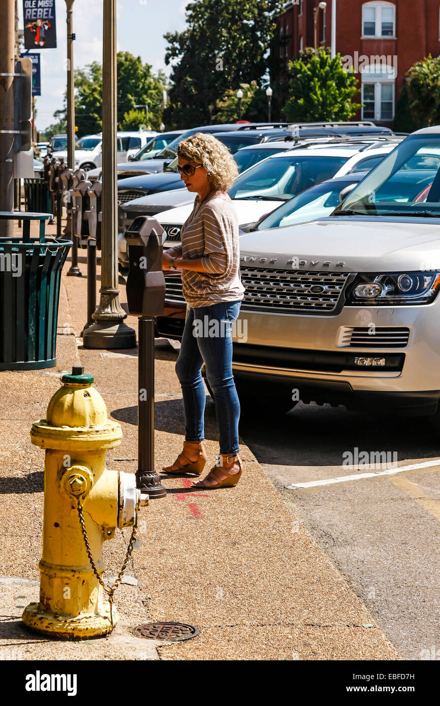 A woman adding coins to a parking meter in Oxford Mississippi Stock Photo