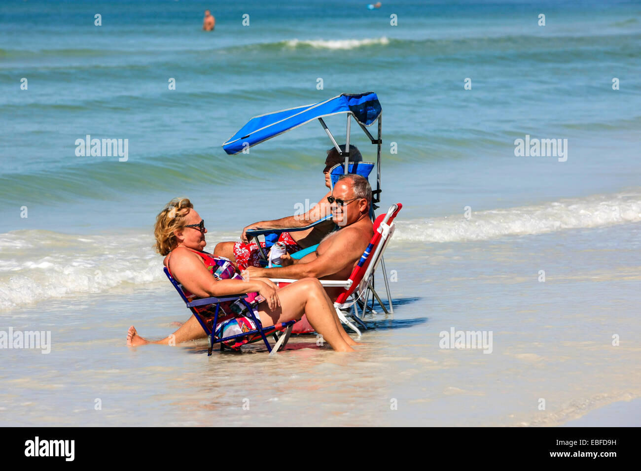 Active seniors sit in a deckchair close to the incoming waters of the Gulf of Mexico on Siesta Key beach in Florida Stock Photo