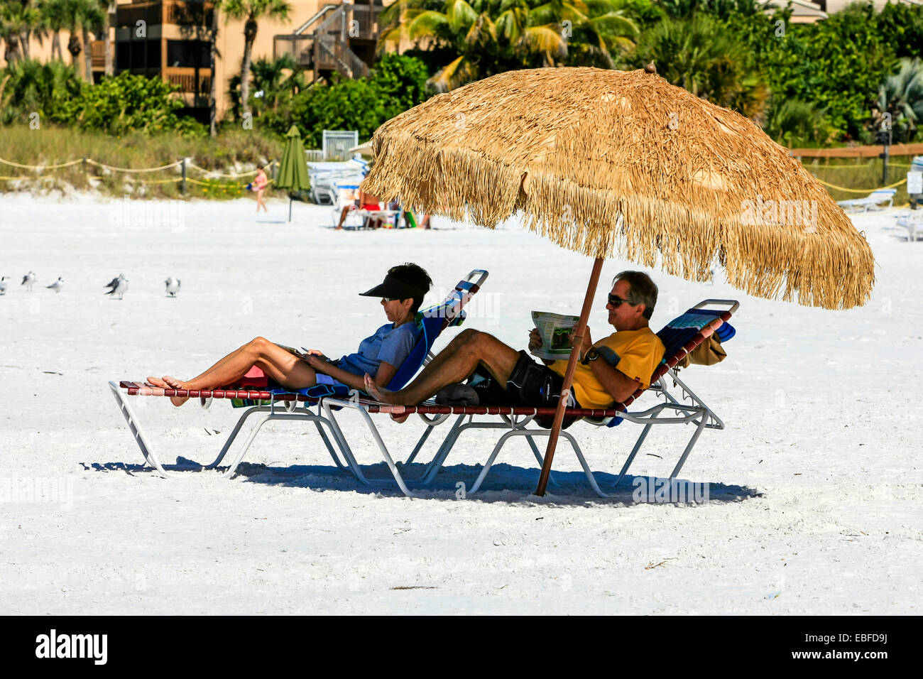 People sit under a rafia umbrella on Crescent beach on Siesta Key Island in Sarasota FL Stock