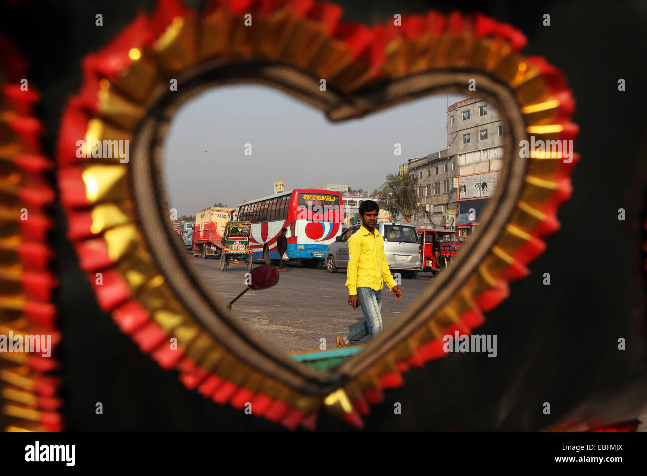 Buses and a man on a street in Dhaka, Bangladesh. They are seen through the heart shape of a rickshaw canopy. Stock Photo