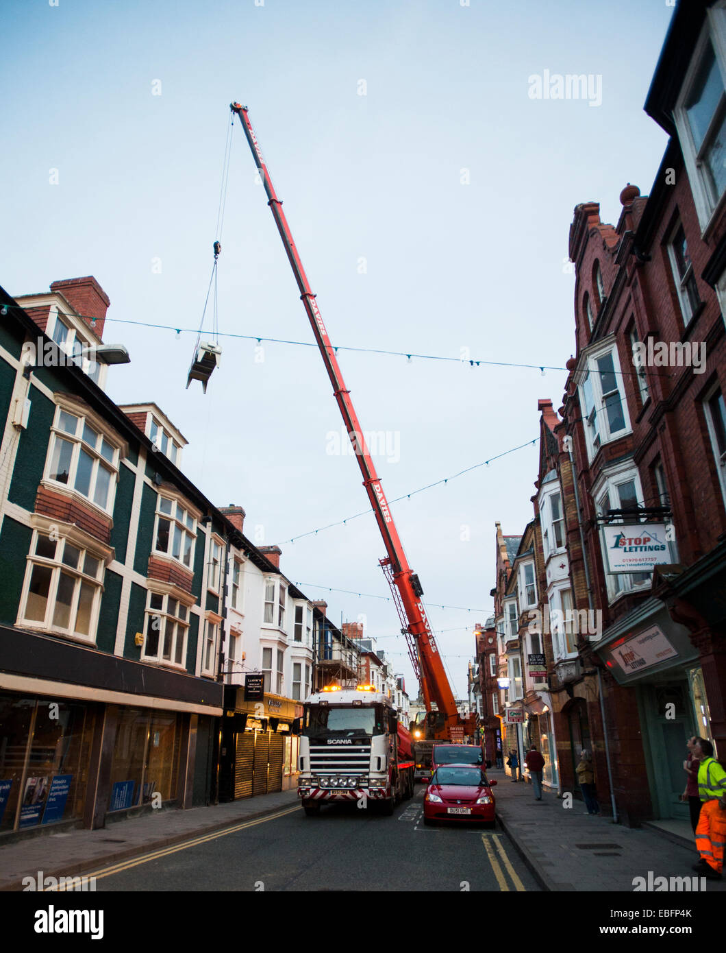 A mobile crane in street Aberystwyth lifting 1 ton air conditioning units over houses and onto a branch of Tesco Express Stock Photo