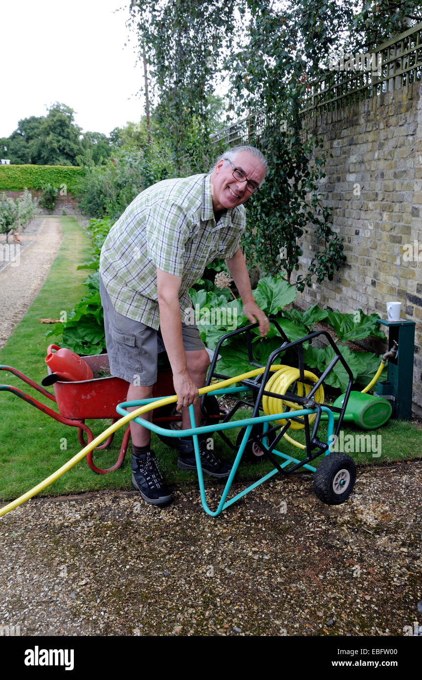 Man winding garden hosepipe onto trolley - volunteer at Chiswick House Kitchen Garden, London Borough of Hounslow Stock Photo
