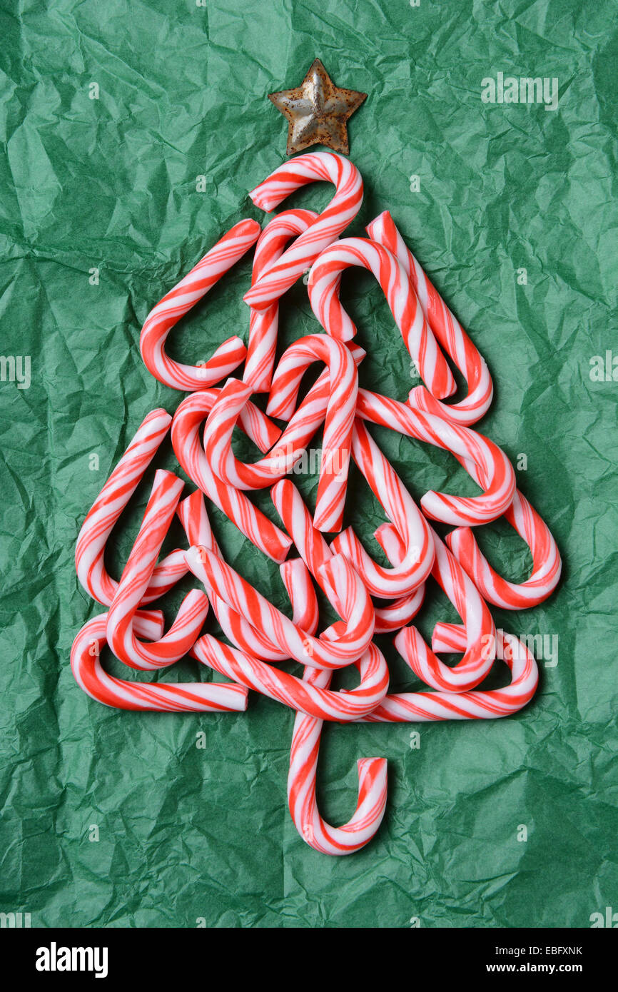 Christmas tree shape made out of candy canes on a green tissue paper surface. A tin star adorns the top of the tree. Vertical Stock Photo