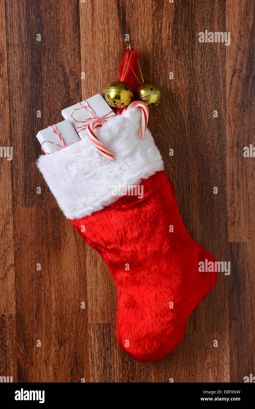 Christmas stocking filled with presents hanging from a hook on a wood wall. Vertical format. Stock Photo