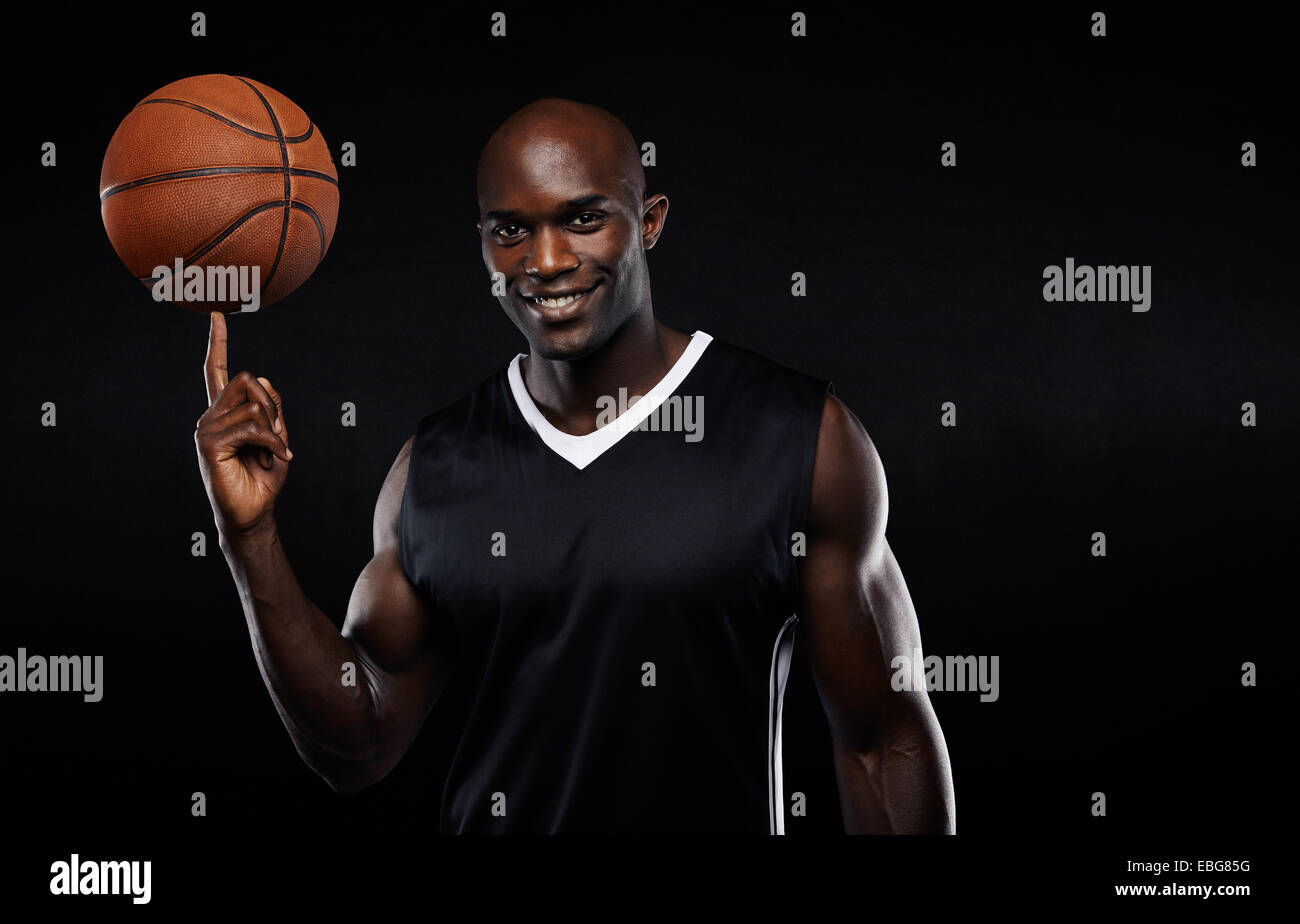 Portrait of happy young African athlete balancing basketball on his finger. Confident basketball player against black background Stock Photo