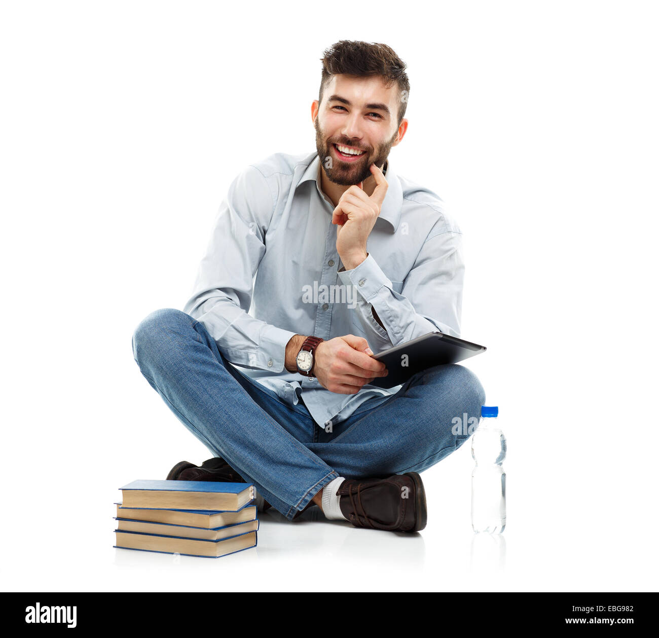 Young bearded smiling man holding a tablet with books and a bottle of water sitting on a white background Stock Photo