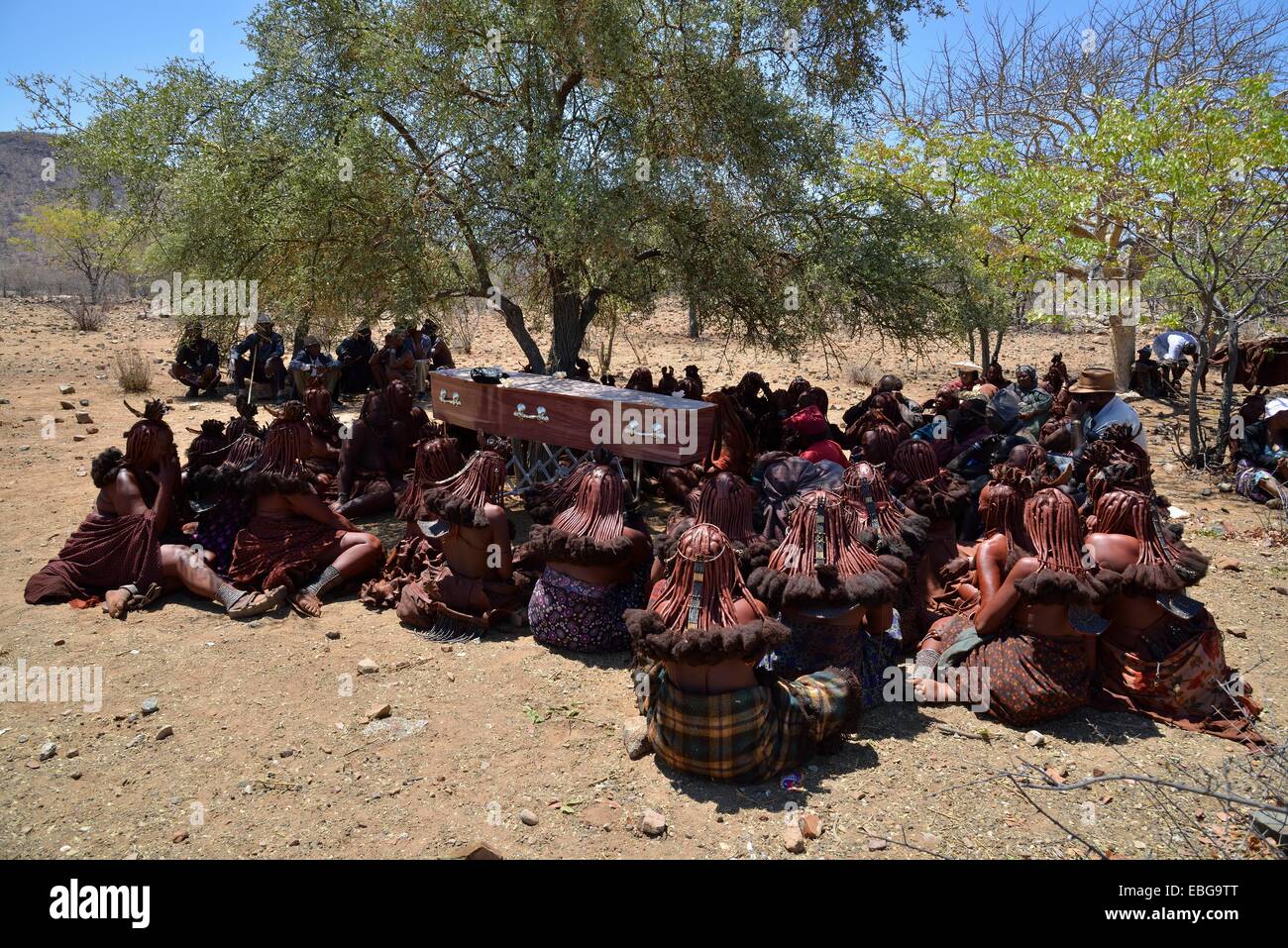 Mourning Himba women sit around the coffin at a funeral, Omohanja, Kaokoland, Kunene, Namibia Stock Photo