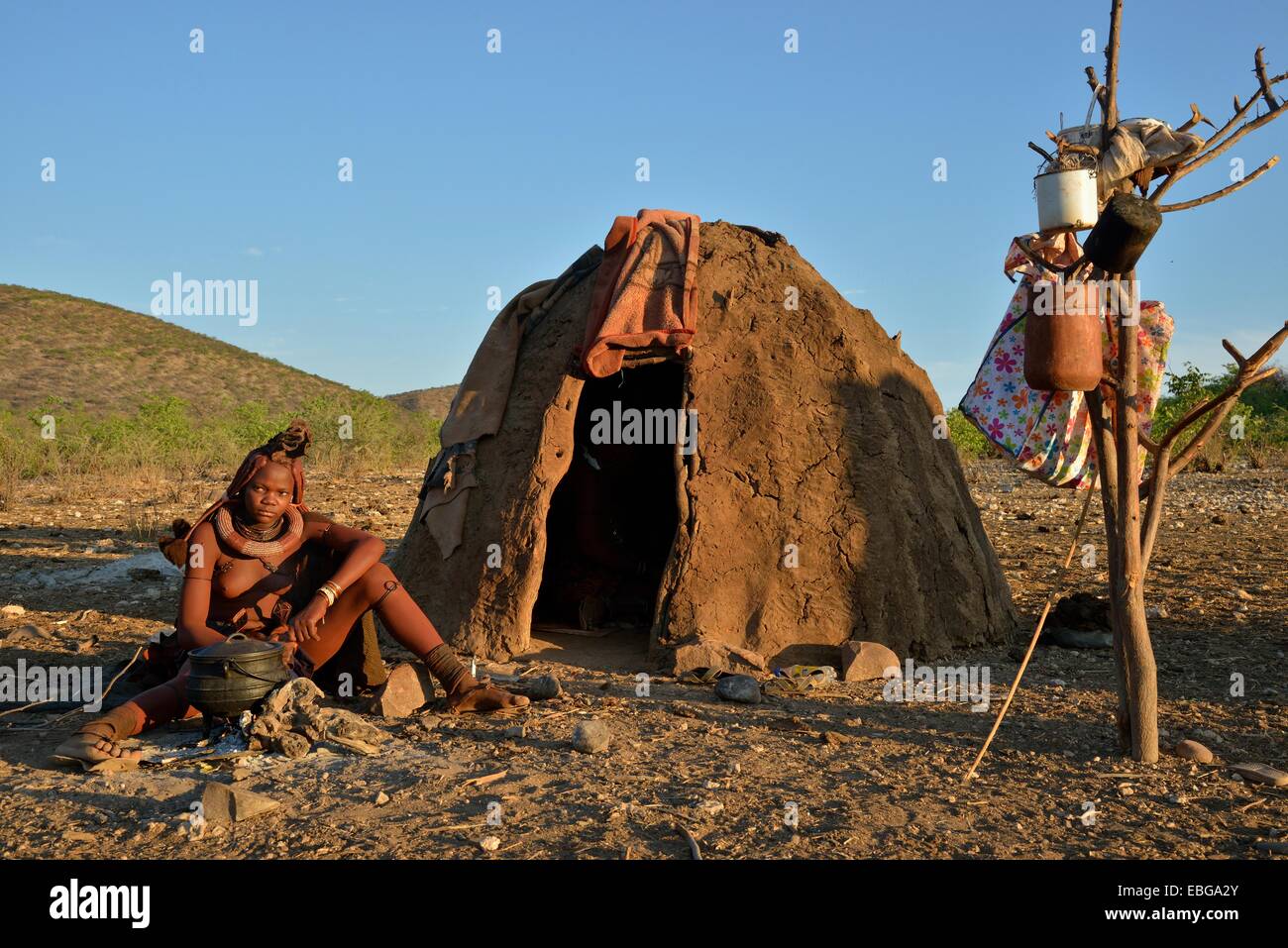 Young Himba woman sitting at a campfire in front of her hut, Ombombo, Kaokoland, Kunene, Namibia Stock Photo