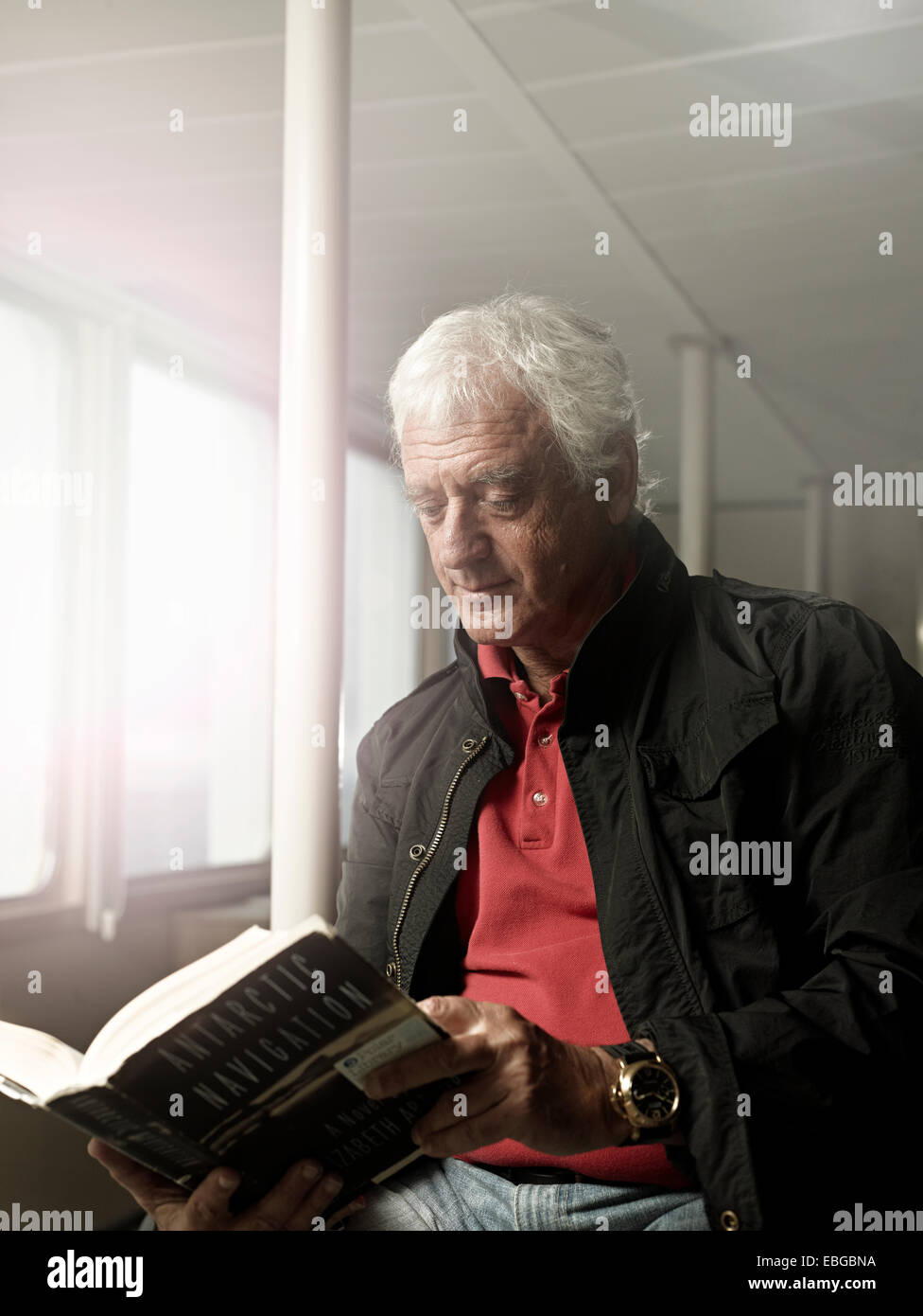 Elderly man reading a book on a ship, Spitsbergen Island, Svalbard Archipelago, Svalbard and Jan Mayen, Norway Stock Photo