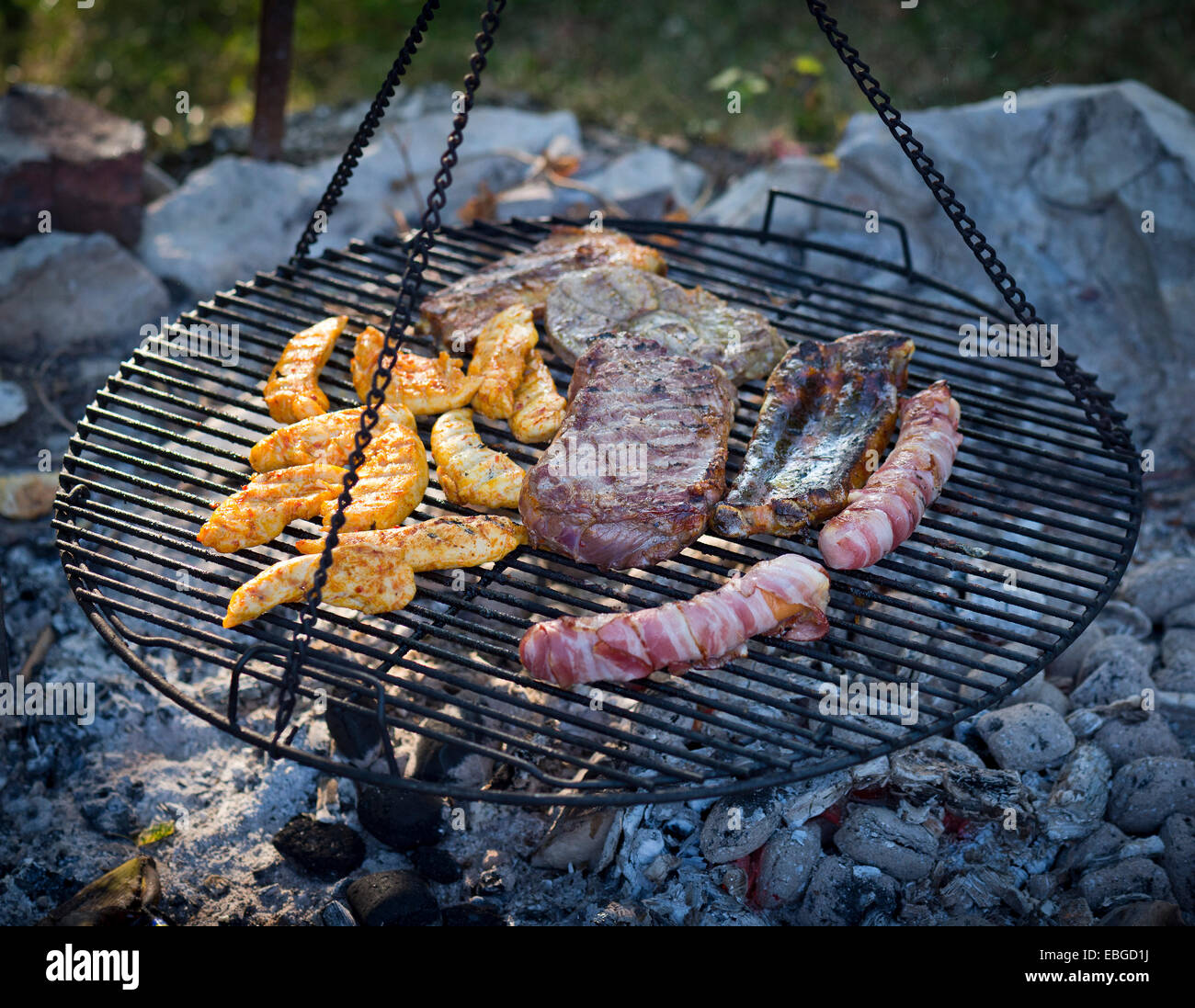 Meat and sausages being cooked on a grill hanging on chains Stock Photo