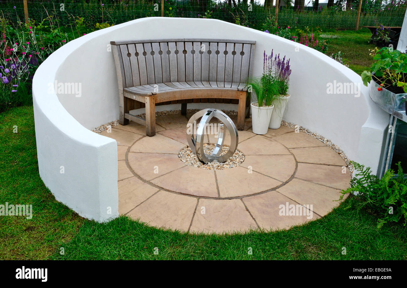 A sheltered circular paved seating area with a small sculpture and planted containers Stock Photo