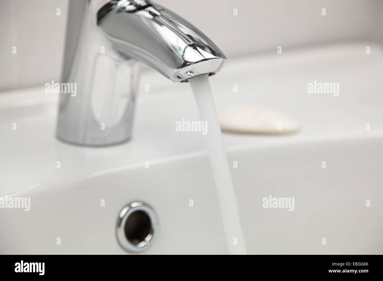 Water tap faucet with flowing water in a white bathroom sink. Stock Photo