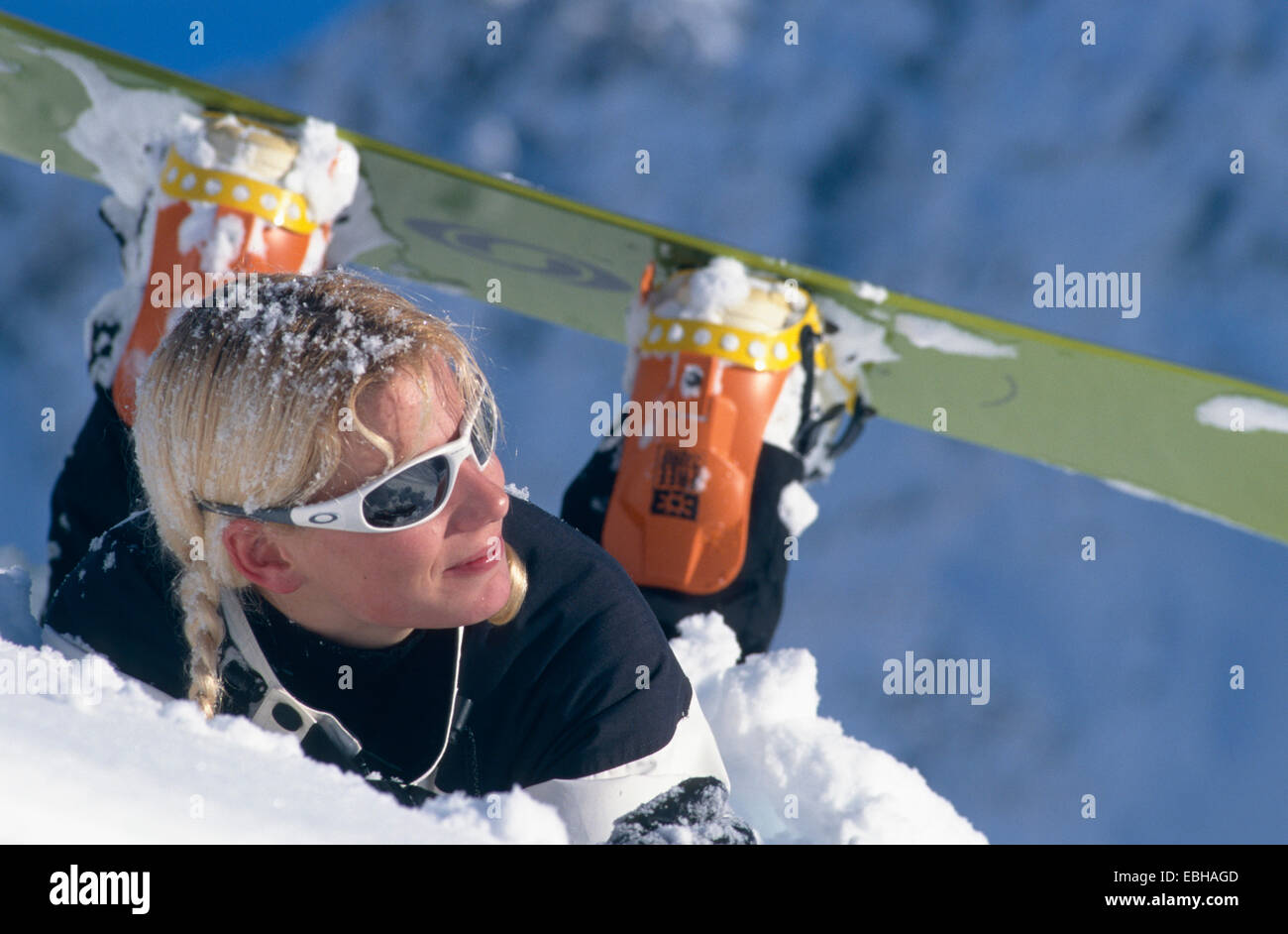 female skier lying in snow, wearing sun glasses, watching sideway. Stock Photo