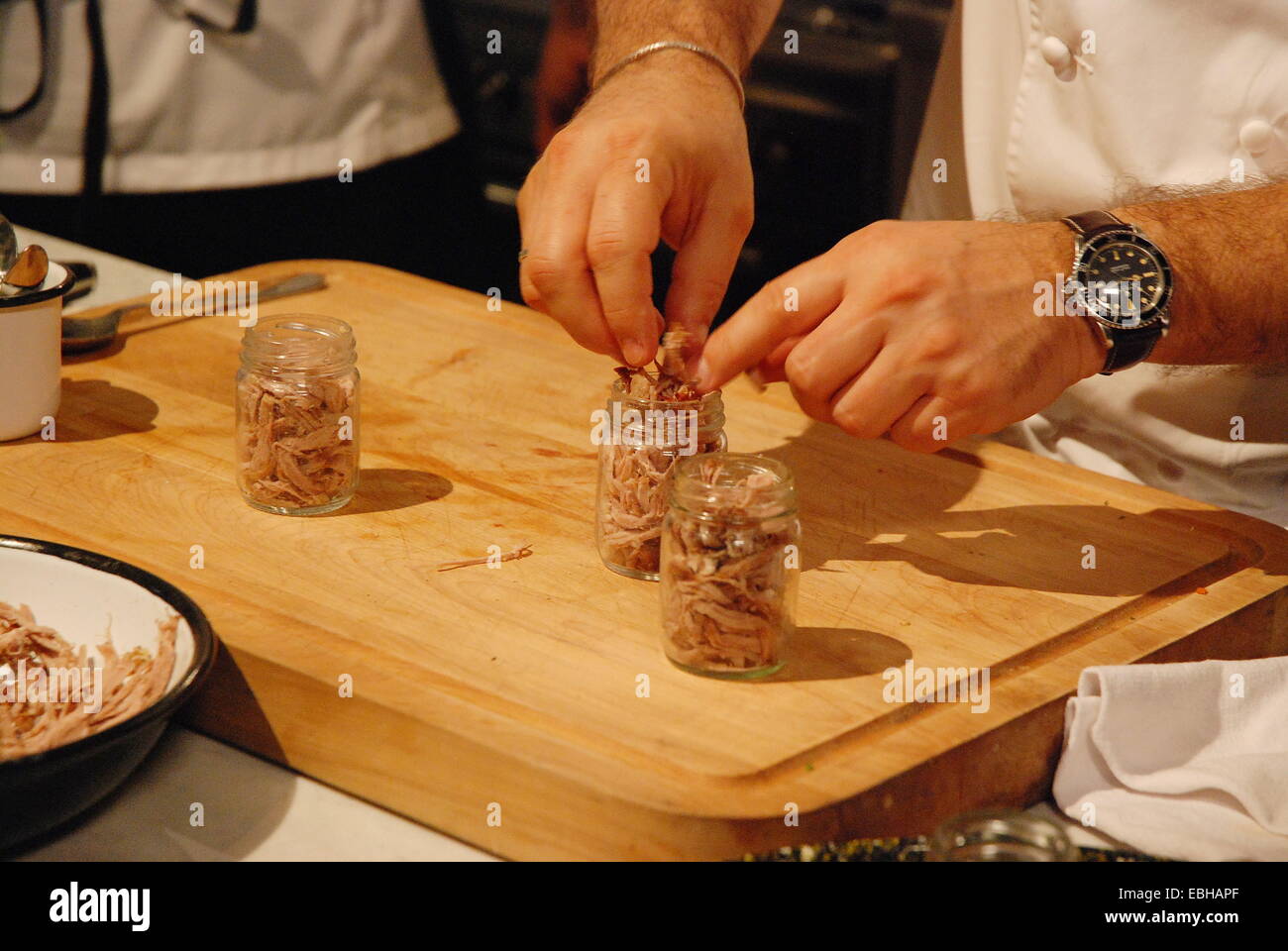 A chef sets portions of sliced duck meat in glass jars to prepare terrine Stock Photo