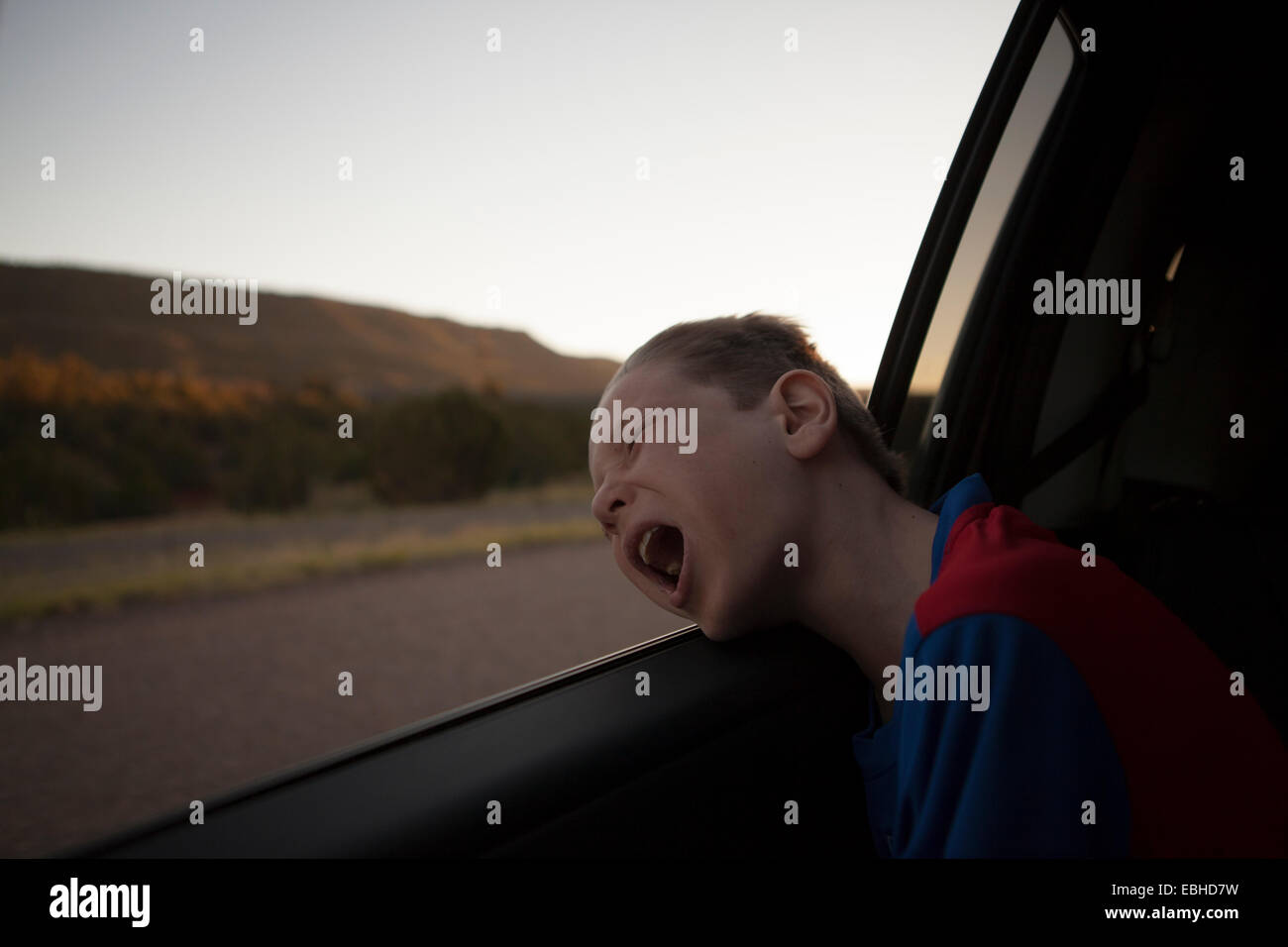 Boy leaning out of car window with eyes closed and mouth open Stock Photo