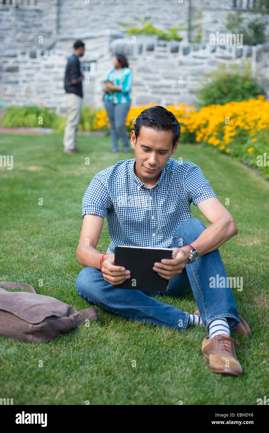 Male student sitting on grass using digital tablet Stock Photo