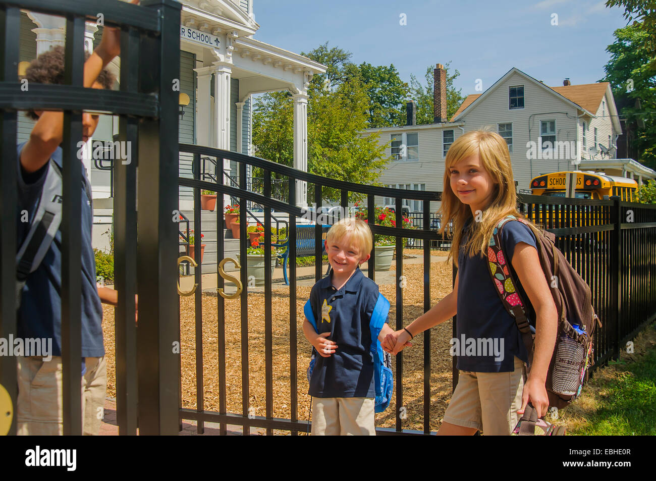 Schoolgirl holding hands with younger brother at school gate Stock Photo