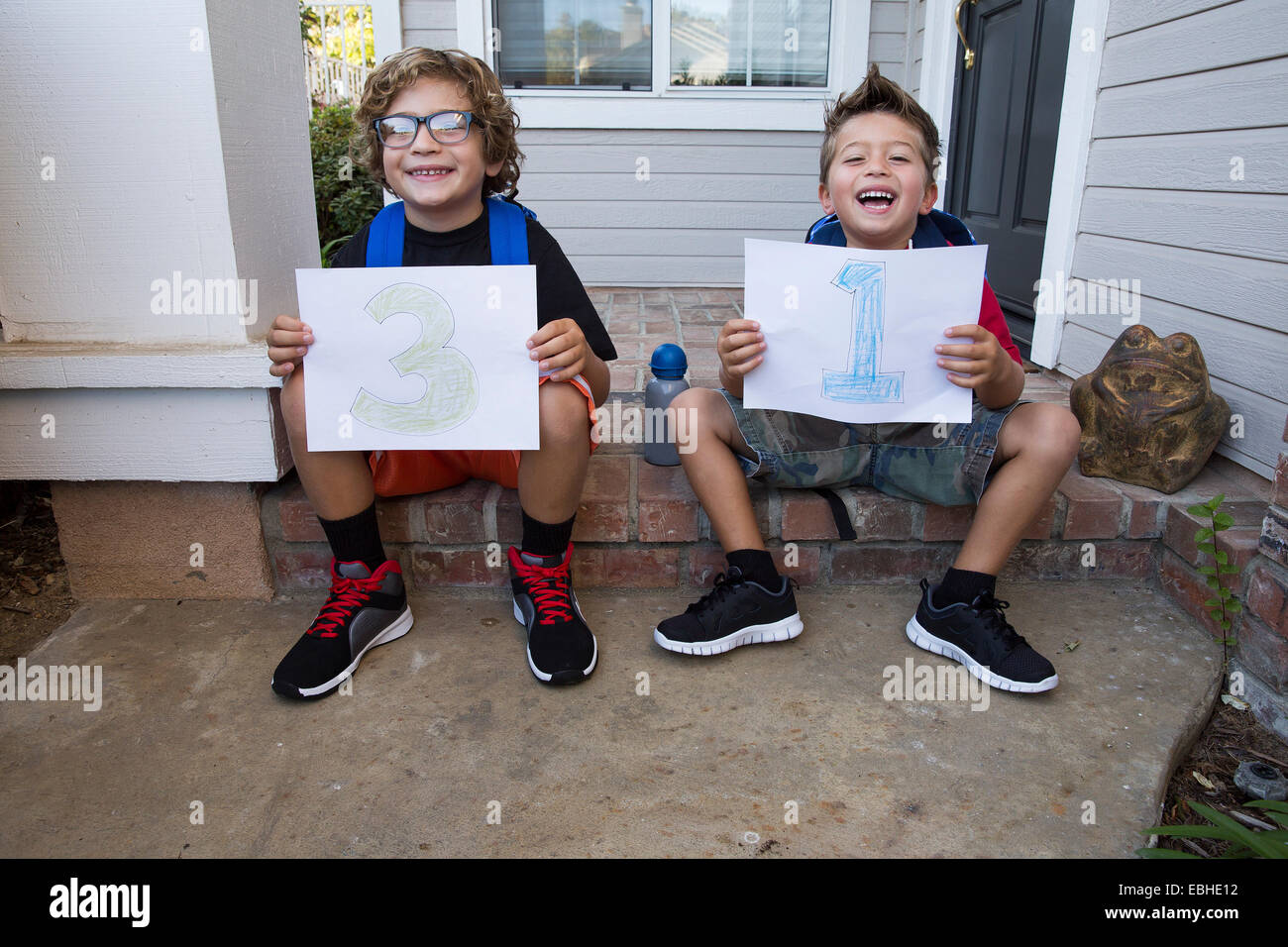 Portrait of two brothers sitting in porch holding up pieces of paper with 3 & 1 Stock Photo