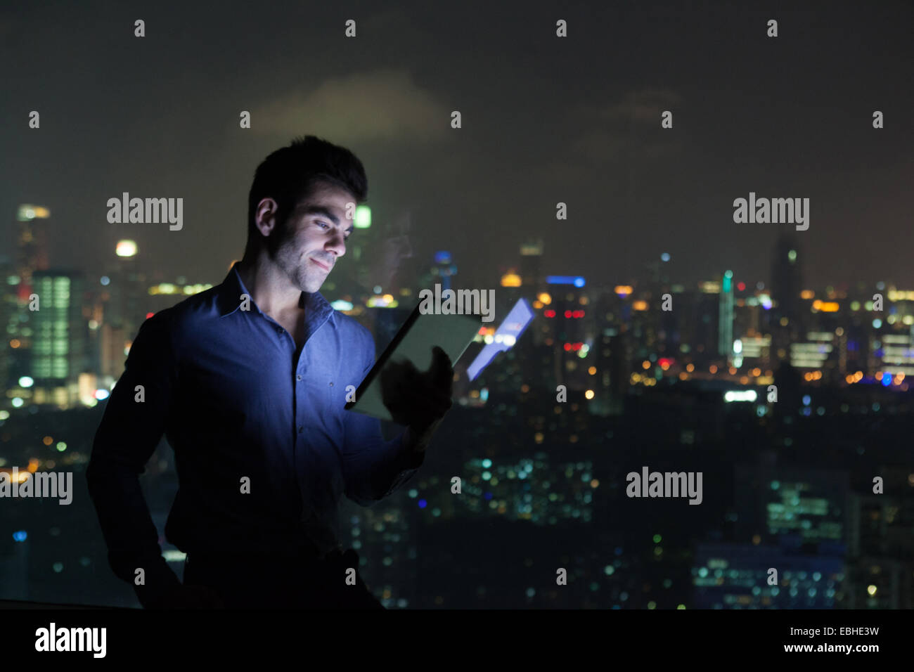 Young businessman looking at digital tablet in front of skyscraper office window at night, Shanghai, China Stock Photo