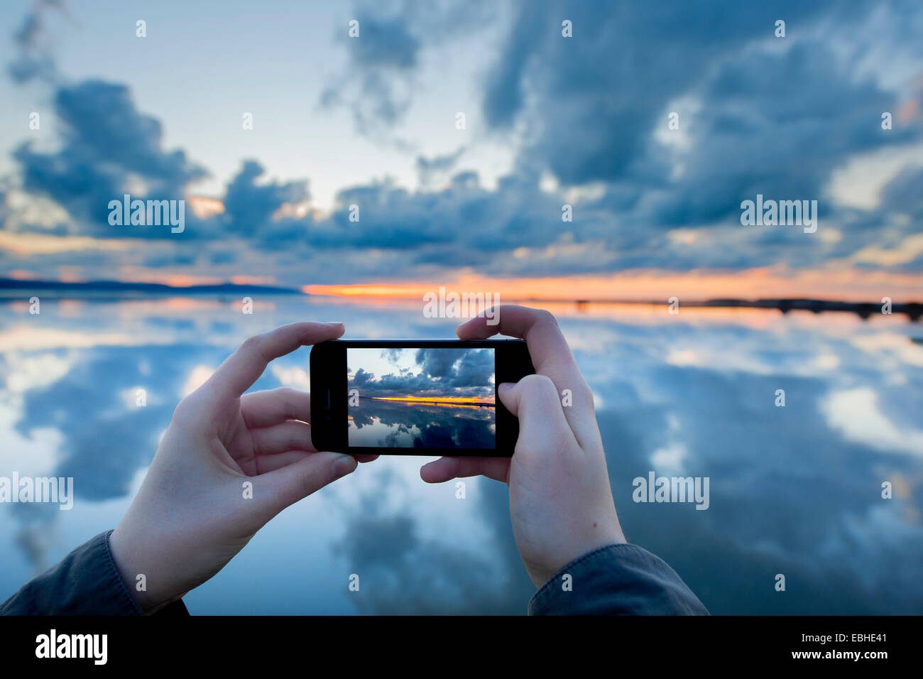 Person photographing reflections on lake with sunset, West Kirby, England, UK Stock Photo