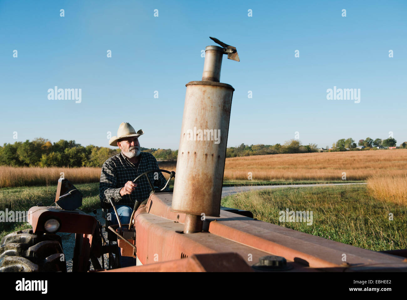 Senior male farmer driving tractor on rural road, Plattsburg, Missouri, USA Stock Photo