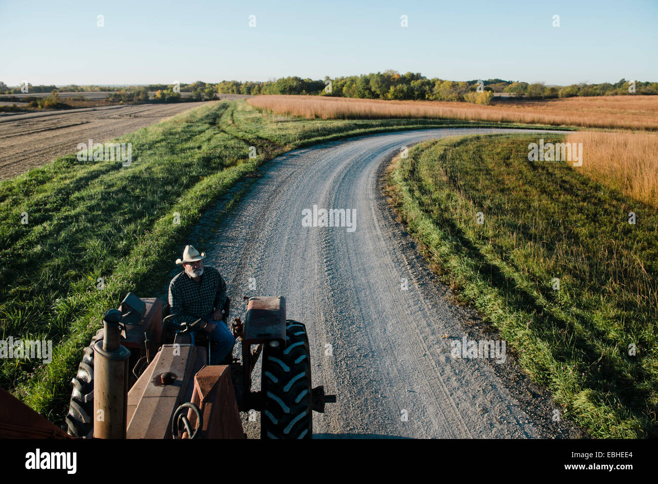 High angle view of senior male farmer driving tractor on rural road, Plattsburg, Missouri, USA Stock Photo