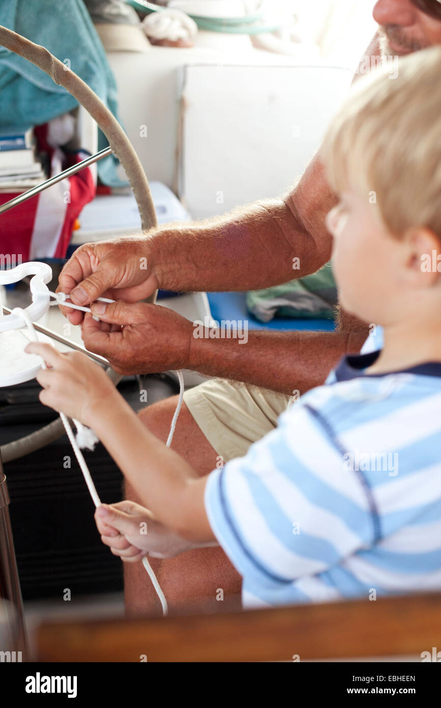 Close up of grandfather and grandson tying knots on sailboat Stock Photo