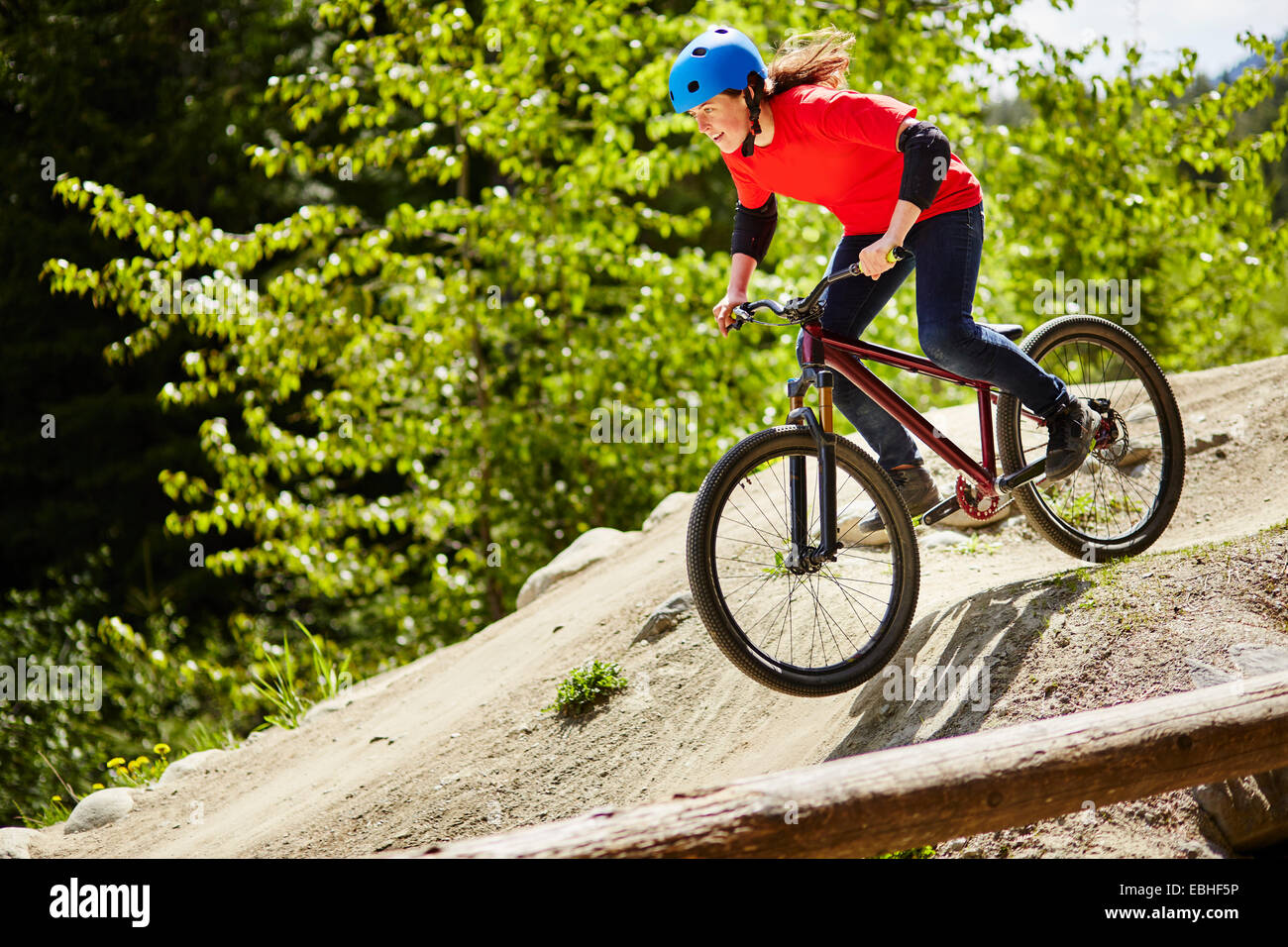 Young female bmx biker speeding down rocks in forest Stock Photo