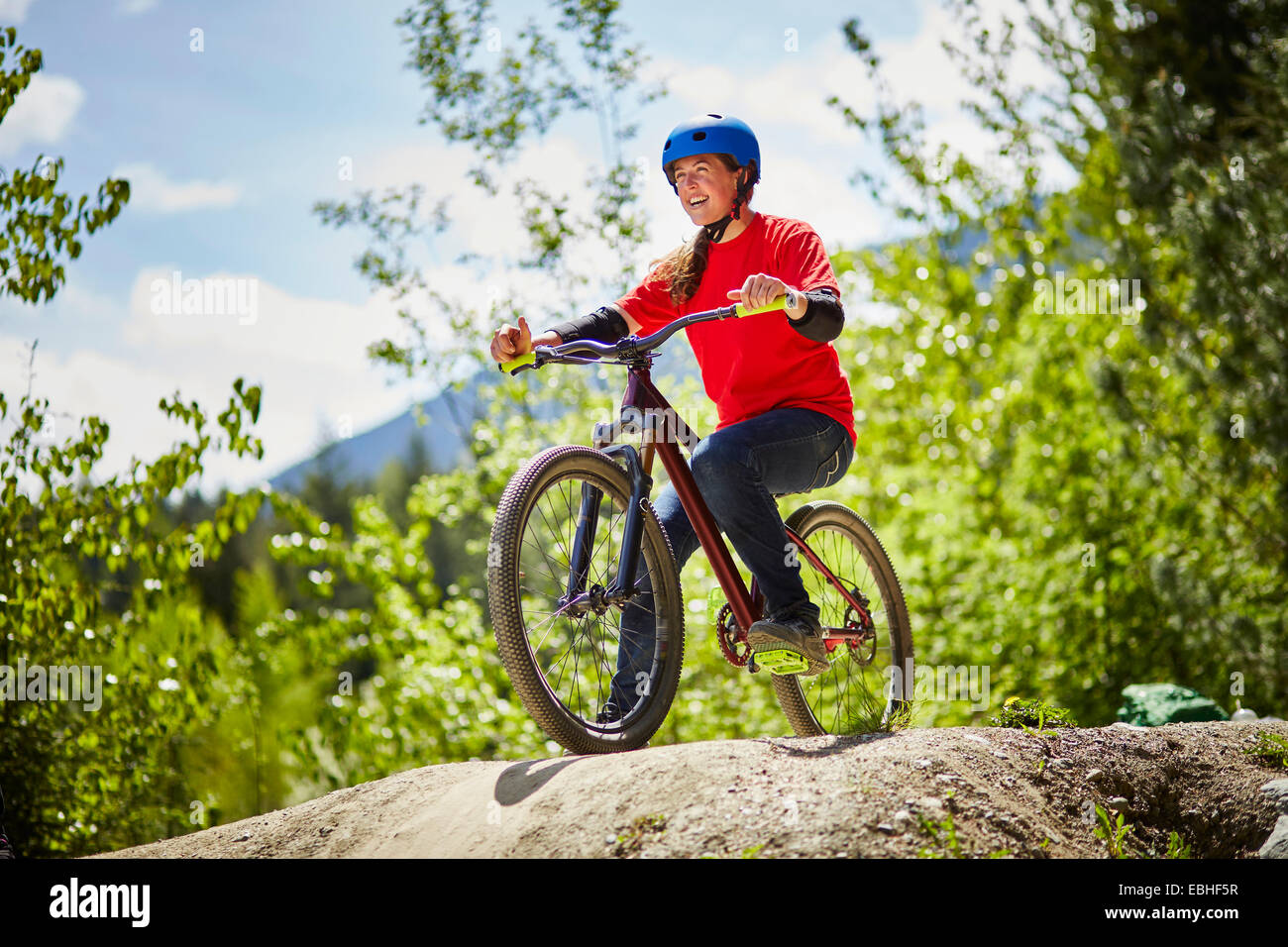 Young female bmx biker poised on edge of rock in forest Stock Photo