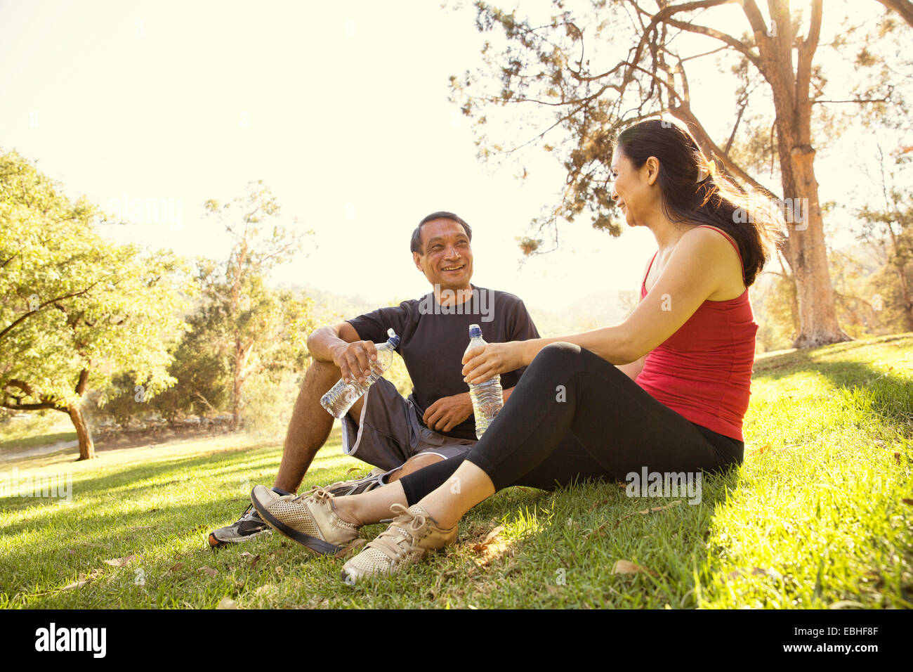 Mature running couple taking a break and drinking water in park Stock Photo