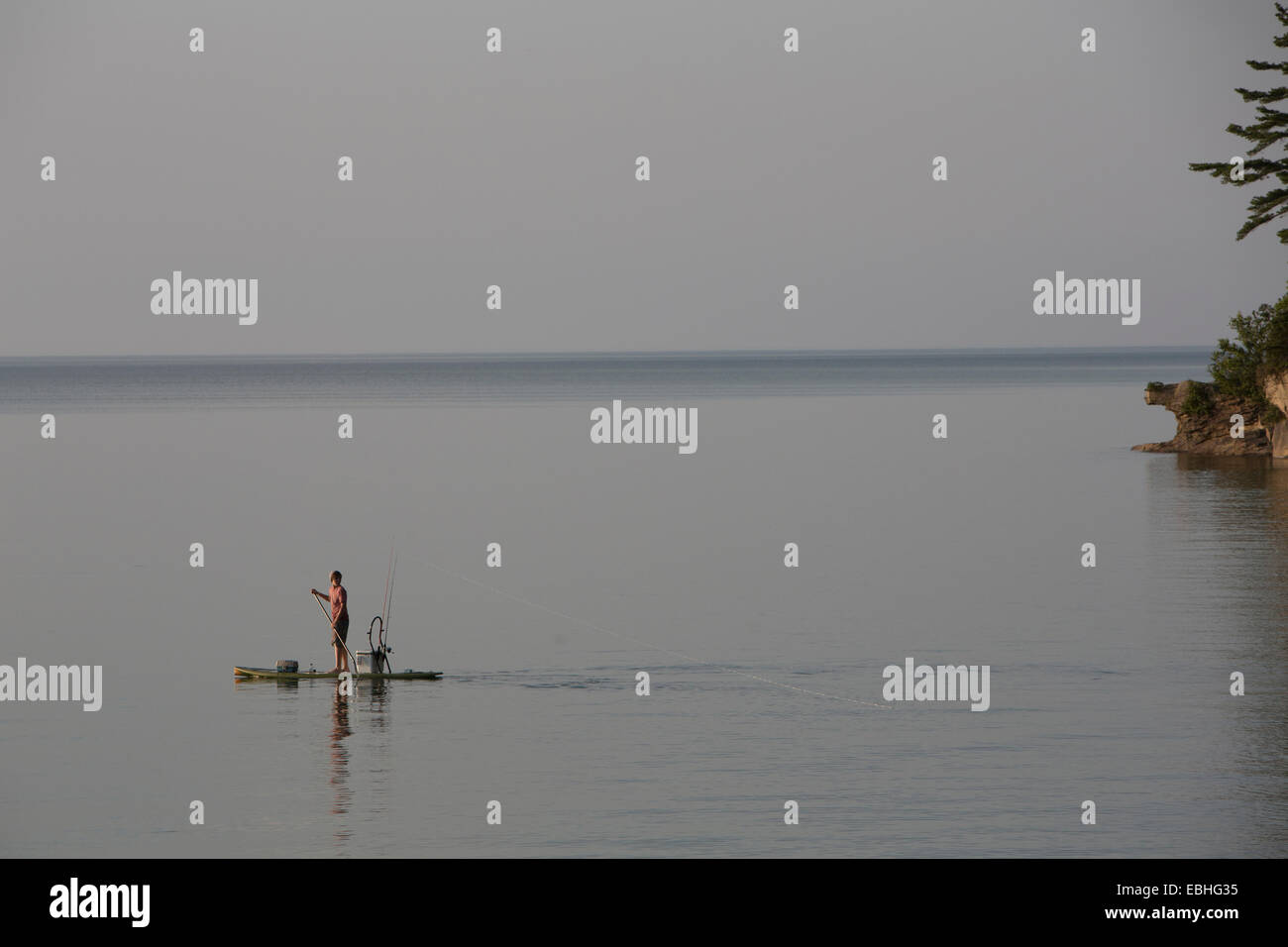 Distant view of teenage boy fishing from paddleboard in Lake Superior, Au Train Bay, Michigan, USA Stock Photo