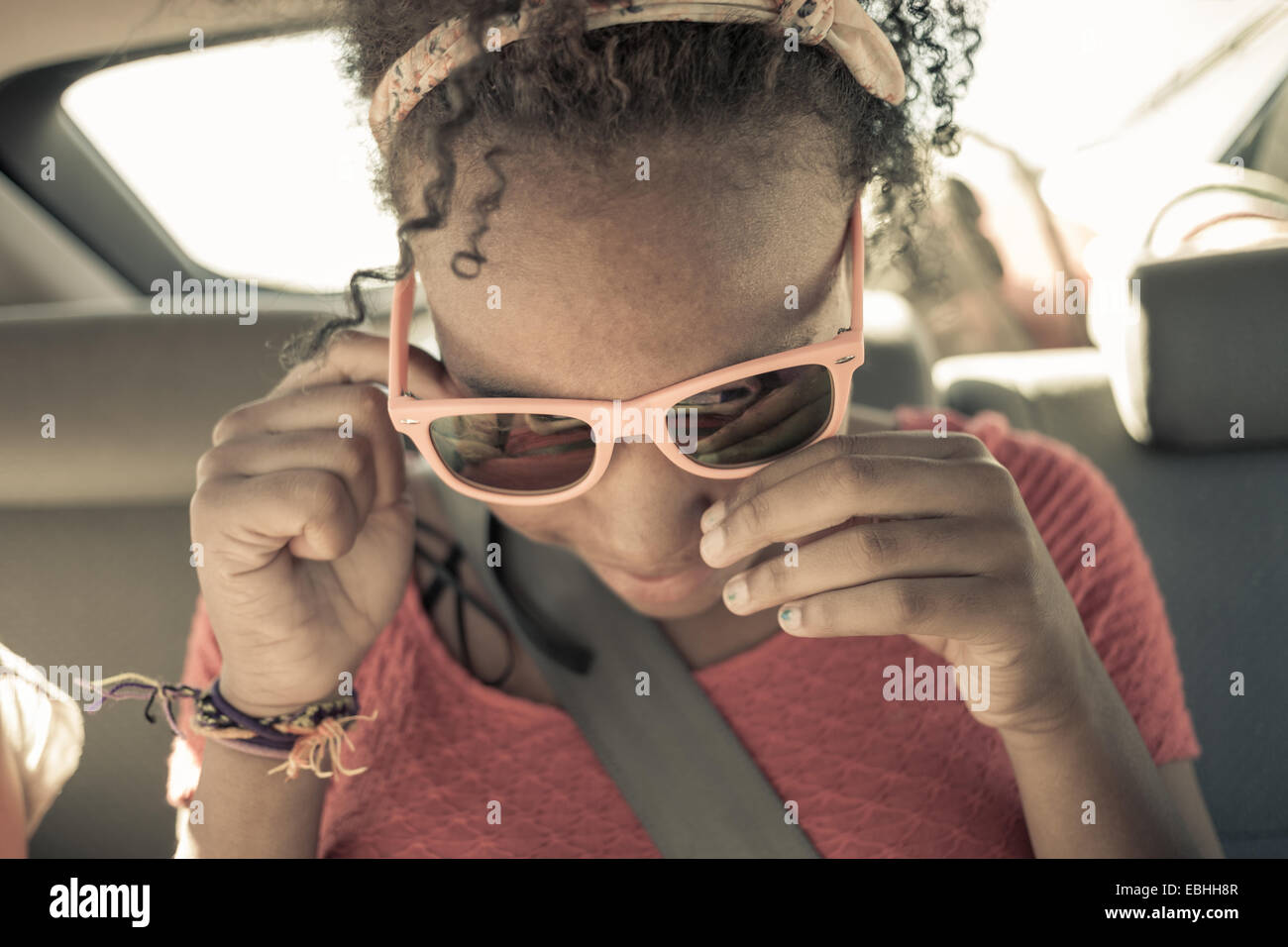 Close up of girl peering though sunglasses on car back seat Stock Photo