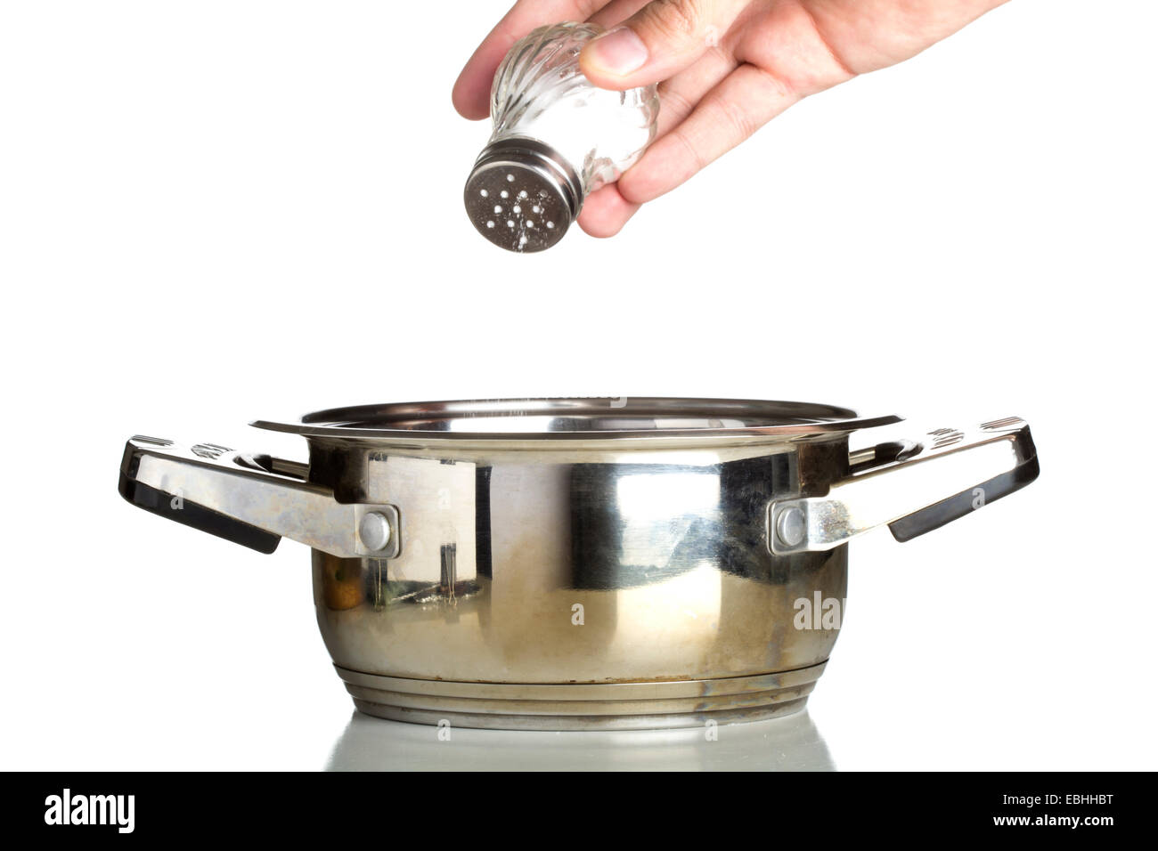 Hand adding salt using salt shaker isolated over white background Stock
