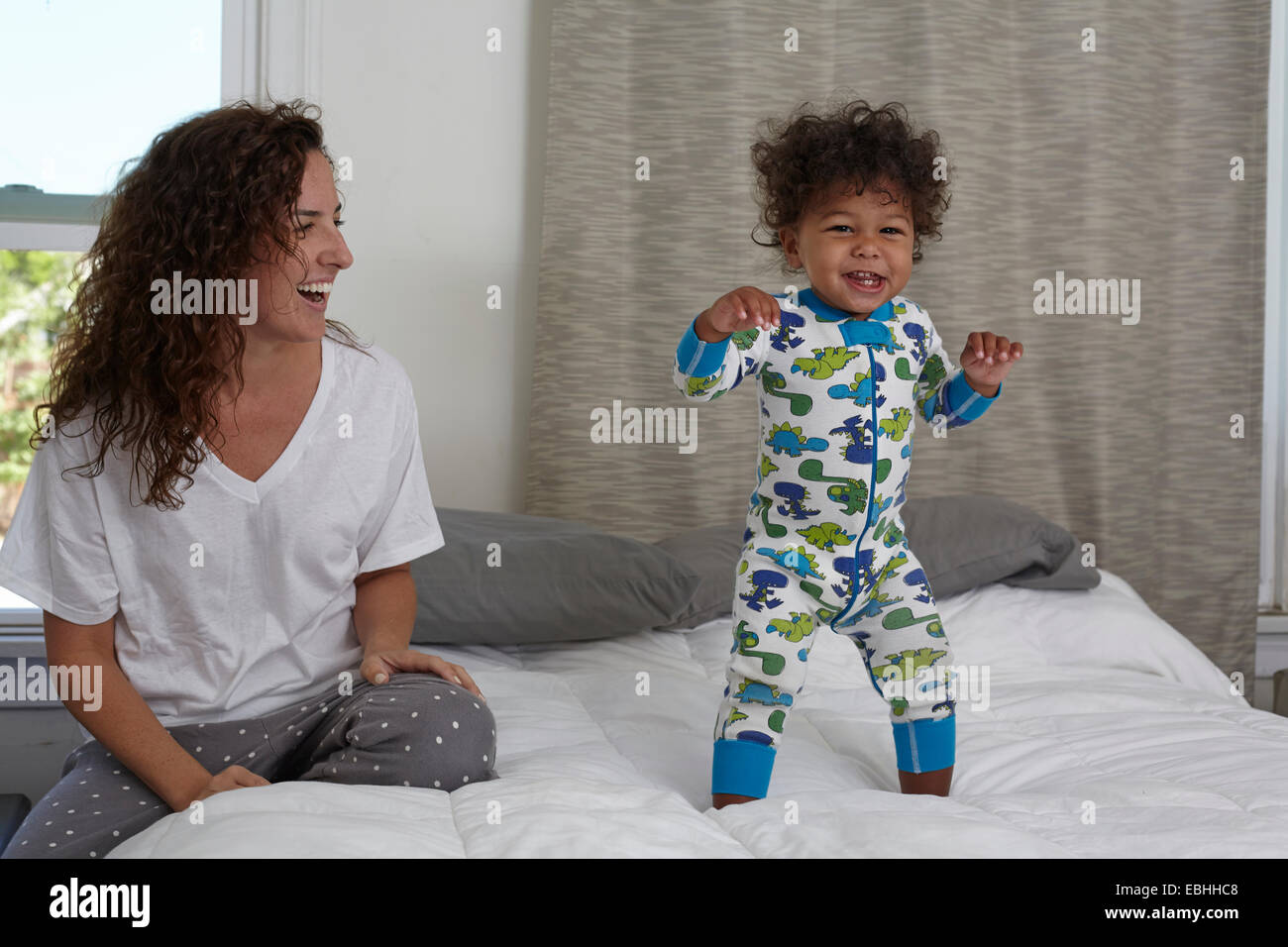 Young woman watching toddler son jumping on bed Stock Photo