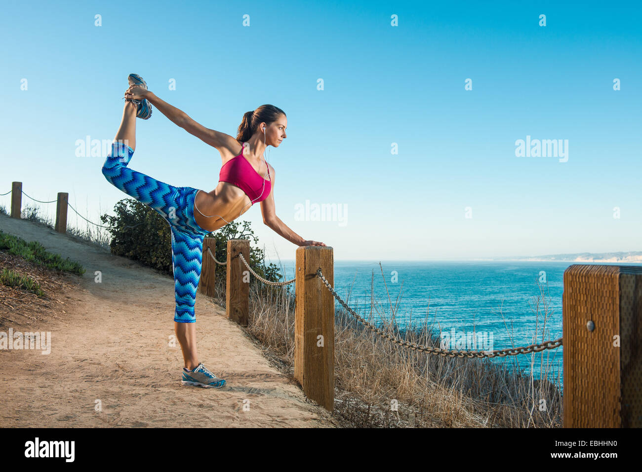 Young woman doing stretches on path by sea Stock Photo