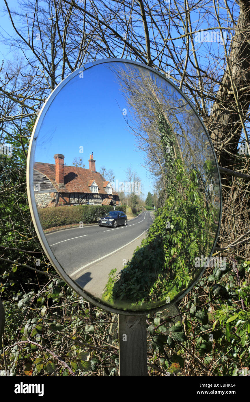 Convex glass safety mirror used to aid exiting concealed drive in country lane. Surrey England UK Stock Photo
