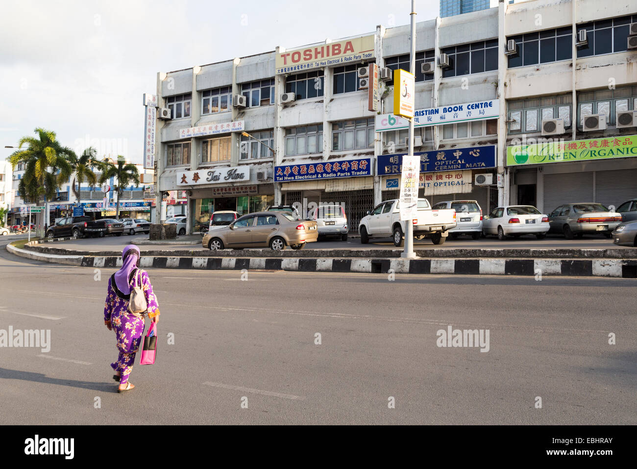 Woman crossing road in front of shops, Miri, Malaysia Stock Photo