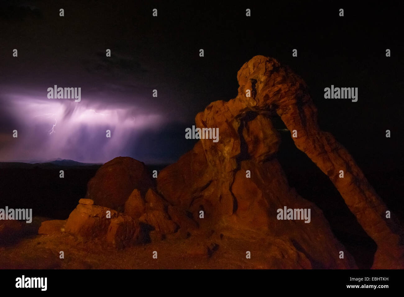 Purple bolt of lightning strikes behind Elephant Rock arch at Nevada's Valley of Fire State Park Stock Photo