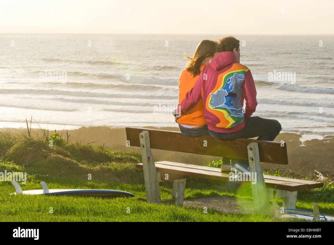 young couple sat on a bench looking out to sea Stock Photo