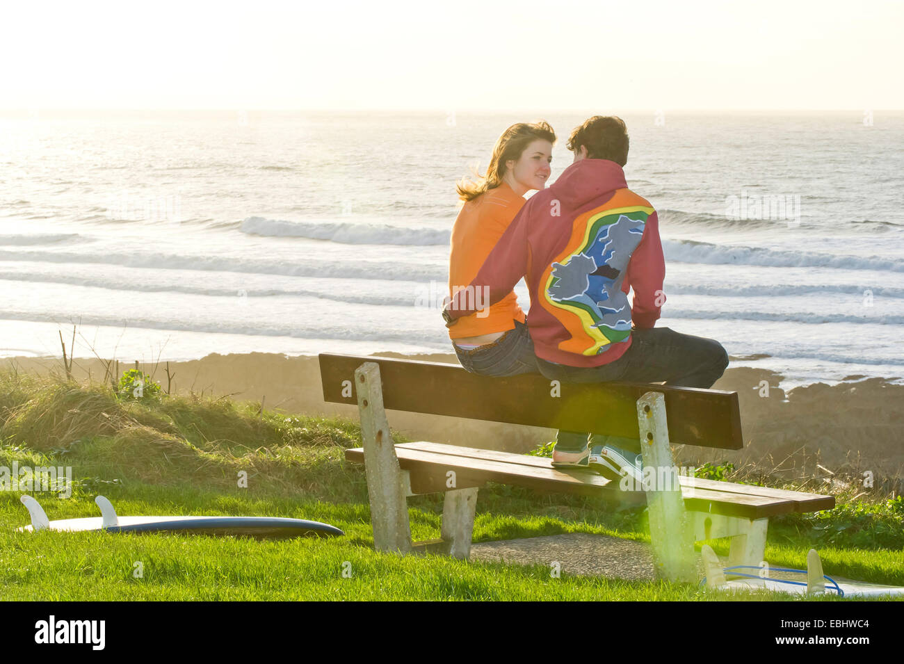 young couple sat on a bench looking out to sea Stock Photo